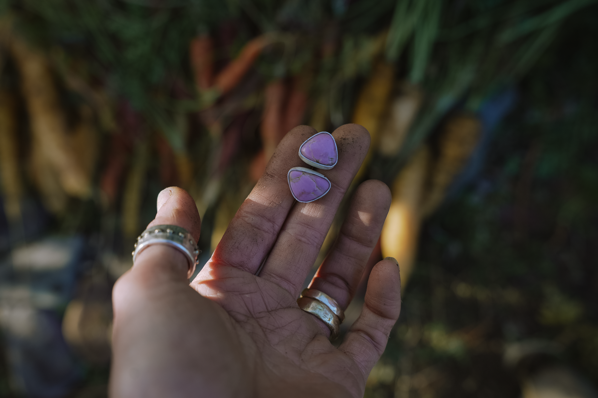 A woman's hand holding two sterling silver and pink phosphosiderite post-style earrings against a blurred natural background.