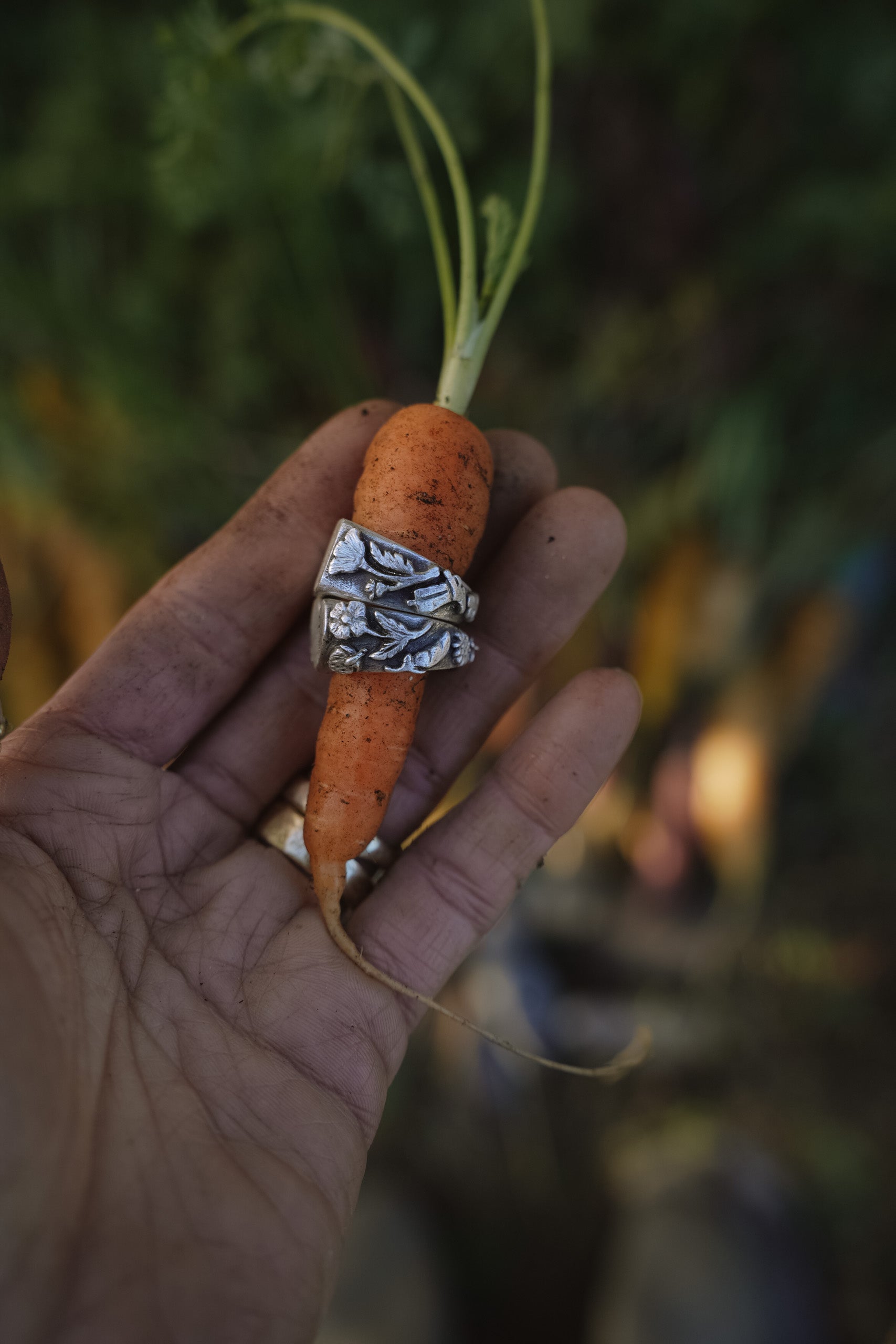 Sterling silver signet rings with carved floral motifs on the band. Shown on a carrot held by a woman's hand against a natural background.
