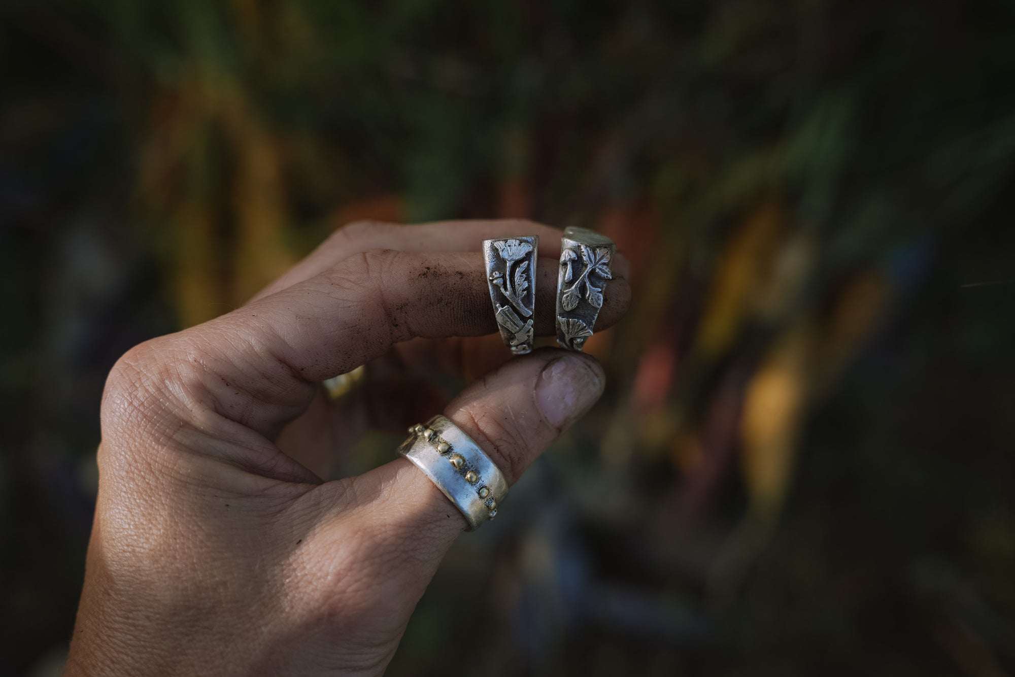 Woman’s hand with two sterling silver signet rings with a carved floral motifs on her forefinger, against a natural background.