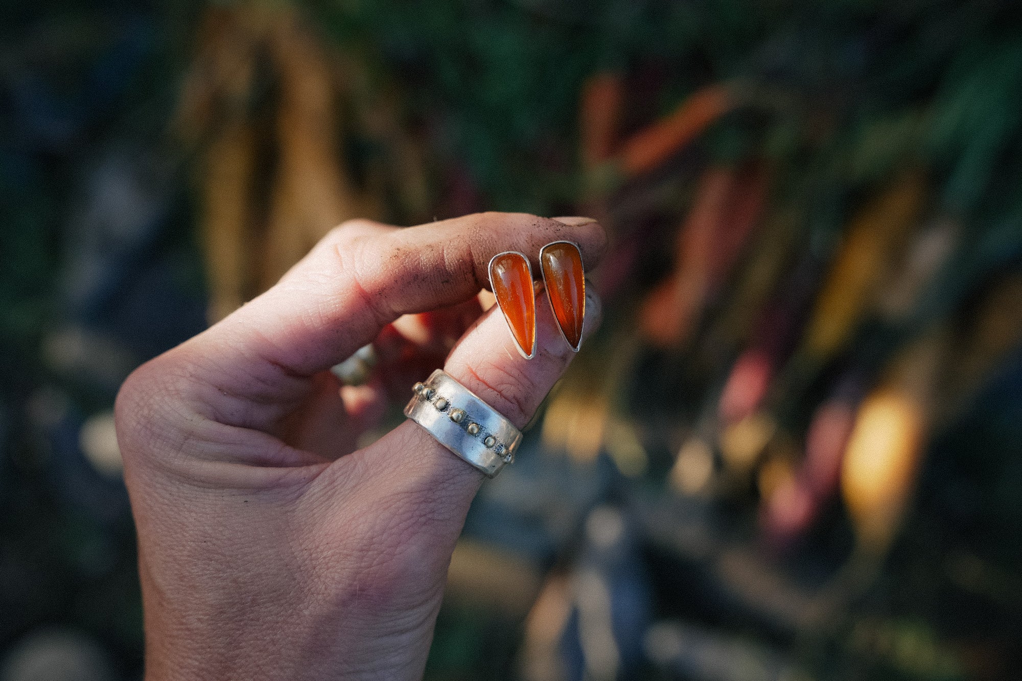Hand holding two sterling silver and chalcedony spike-shaped earrings against a blurred natural background
