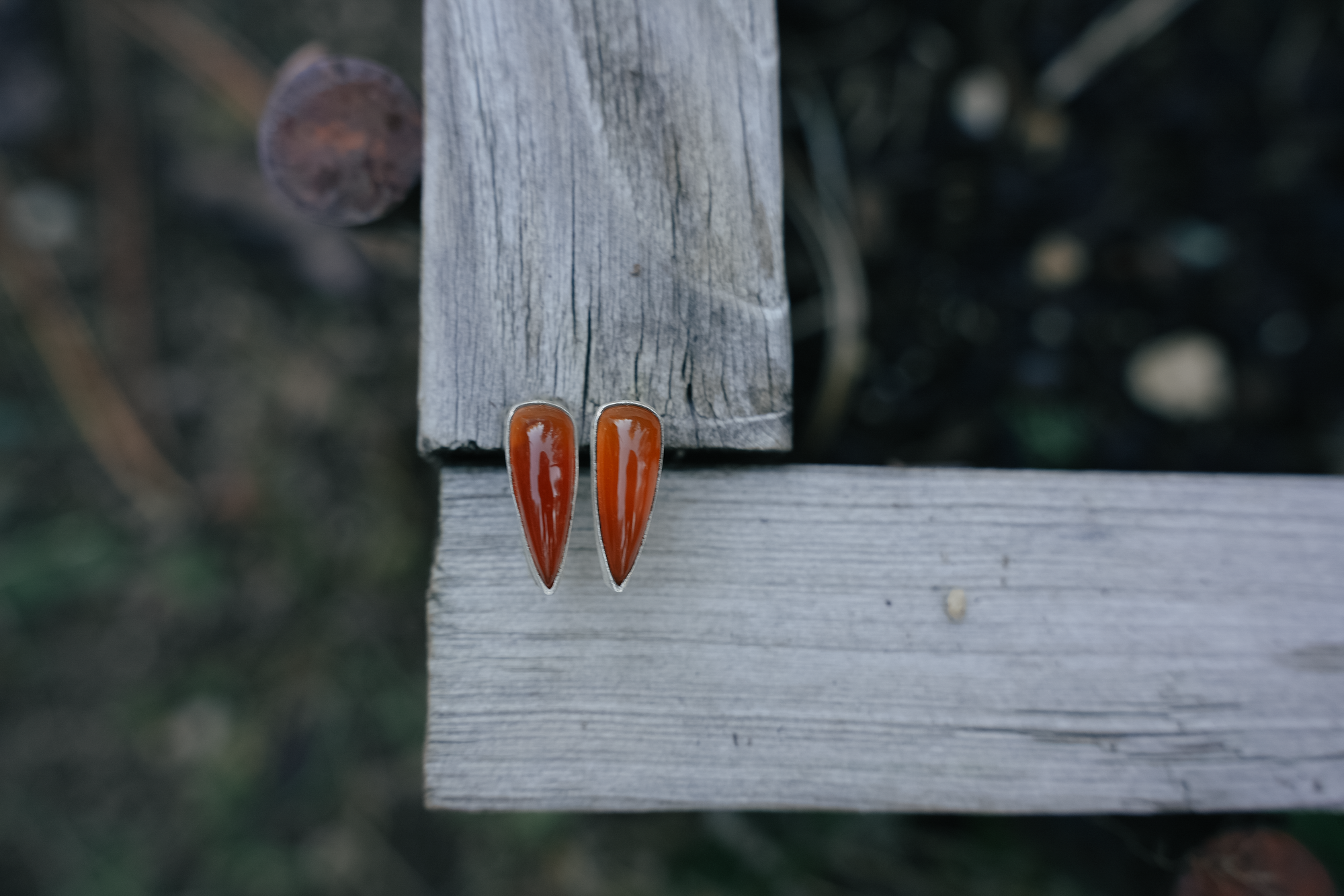 Teardrop-shaped sterling silver and chalcedony earrings on a wooden surface with a blurred natural background