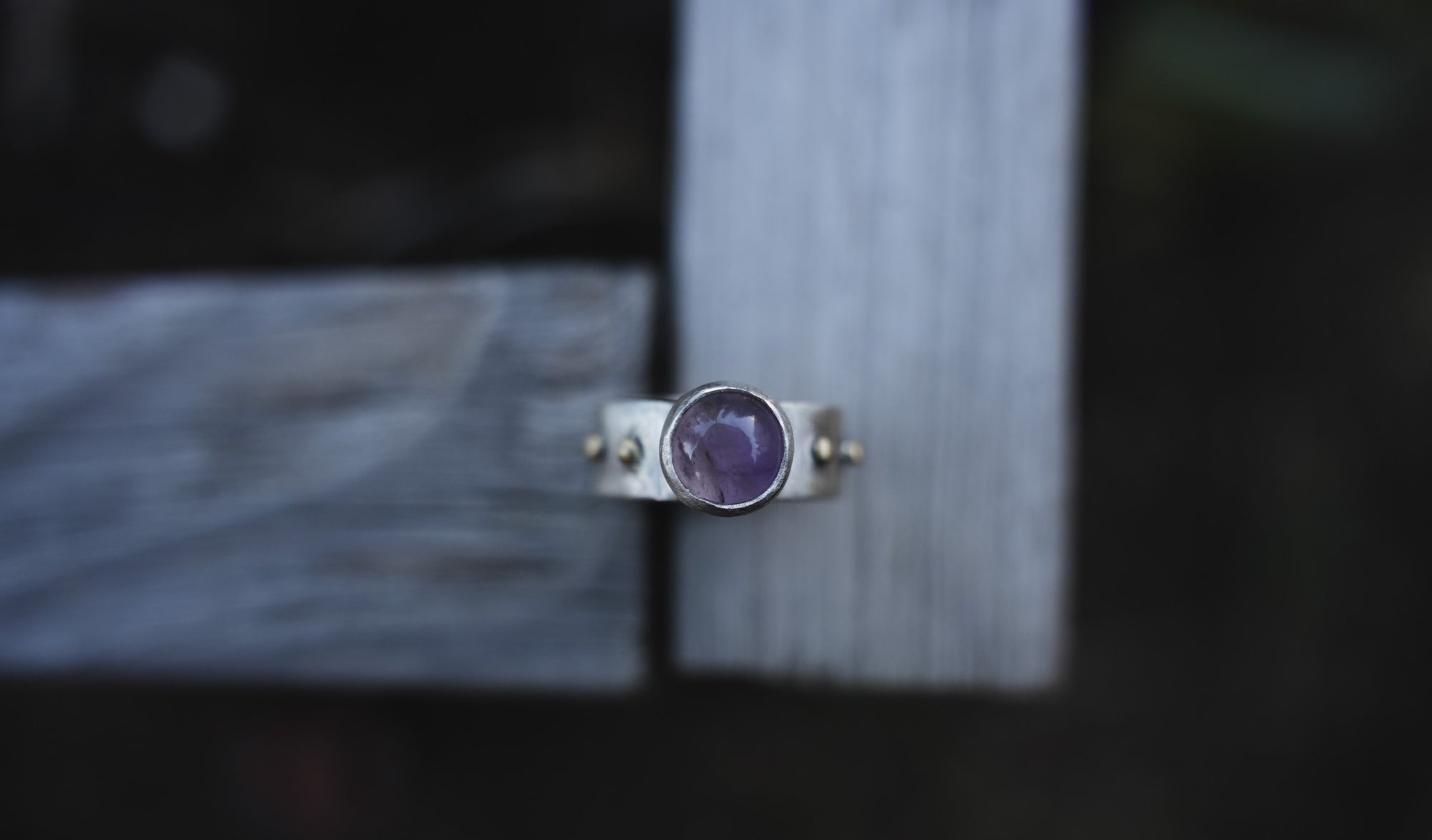 A sterling silver and 18K gold ring with a purple amethyst gemstone against a blurred wood background.