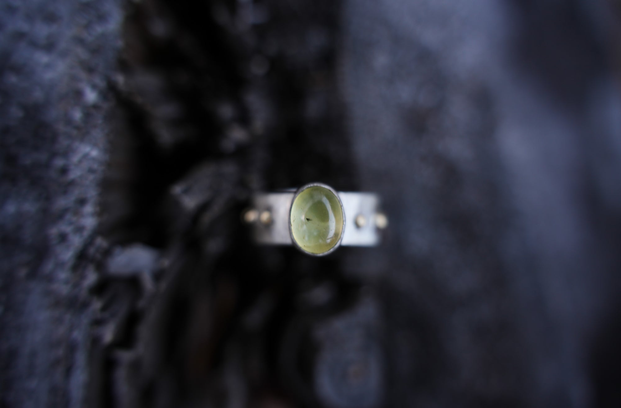 Sterling silver and 18K gold ring with a light green citrine gemstone against a textured black background.