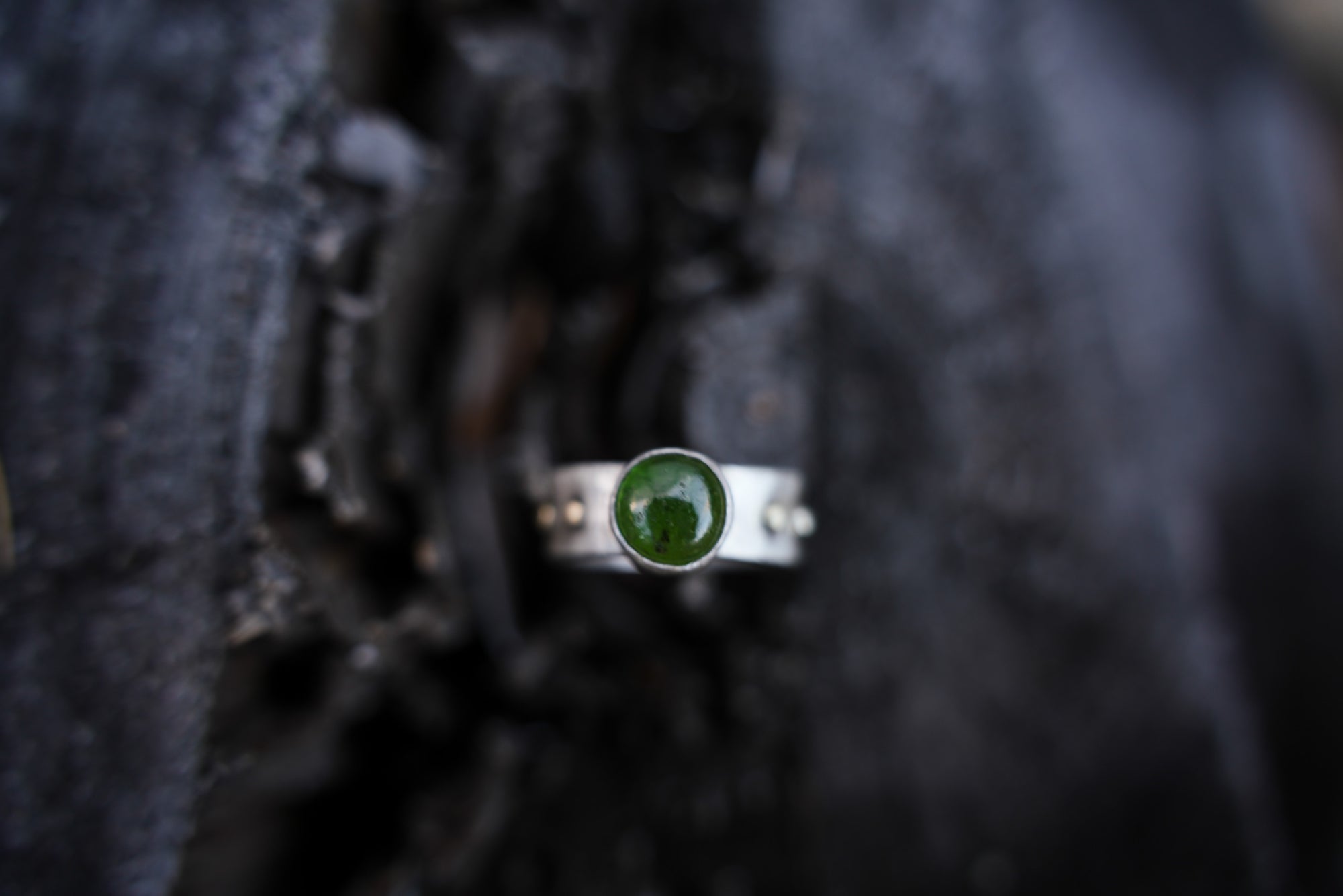 A sterling silver and 18K gold ring with a dark green vesuvianite gemstone against a dark, blurred background.