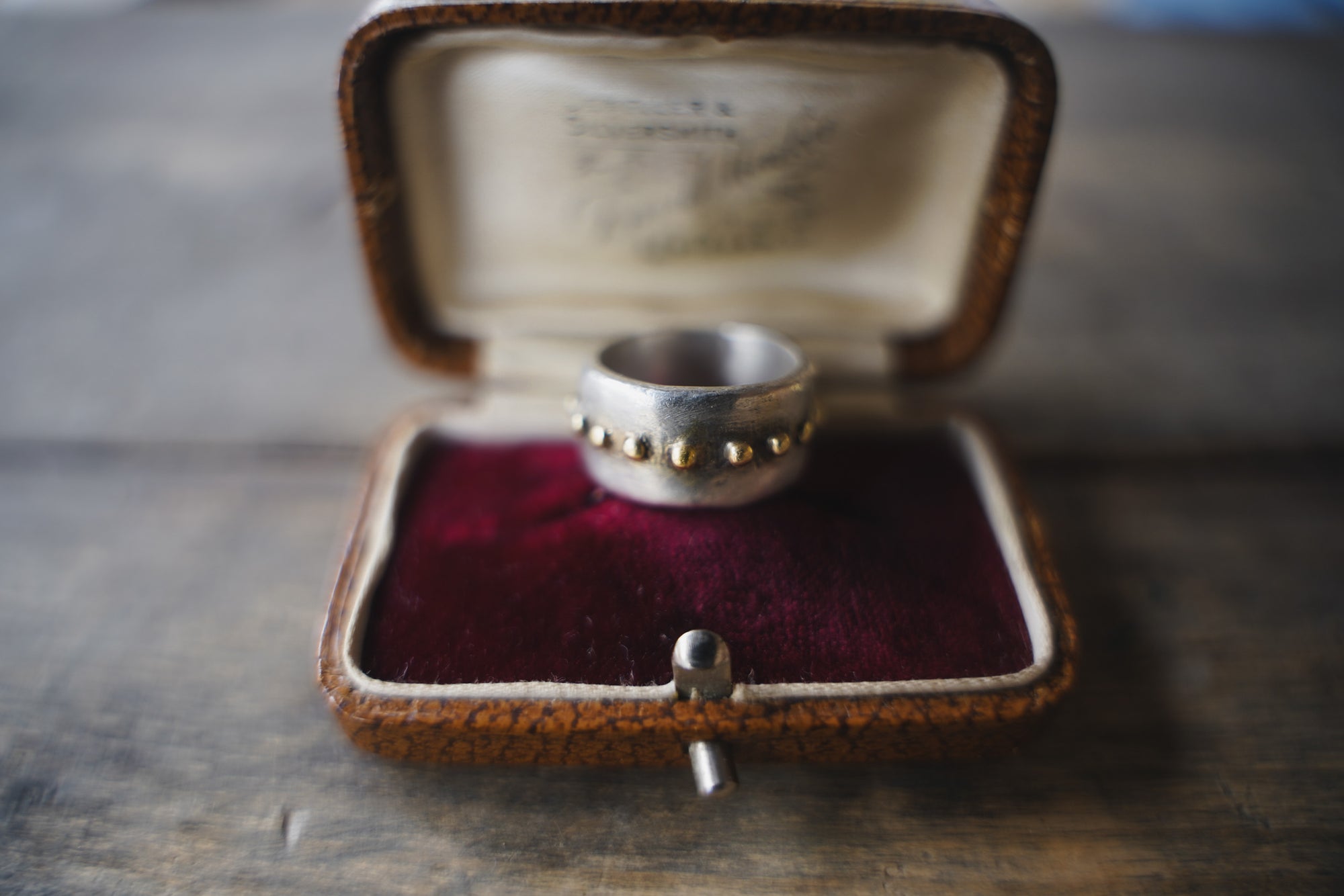Close up of an antique snakeskin and burgundy velvet jewelry box with a sterling silver wide-band ring with a line if 18K gold beads around the circumferance.