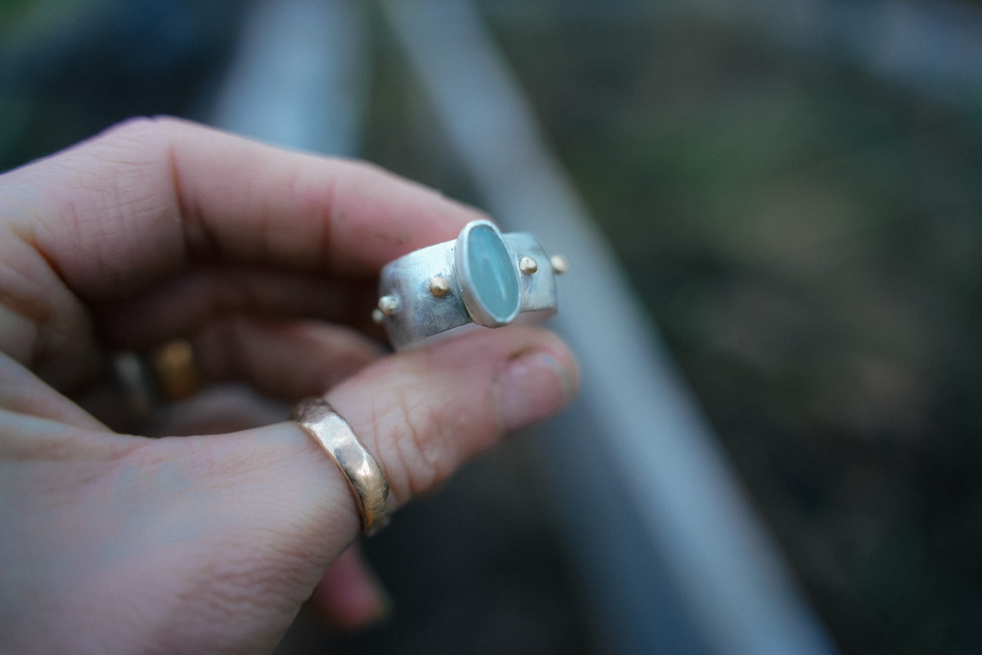A woman's hand holding a sterling silver ring with a blue aquamarine oval stone against a blurred background.