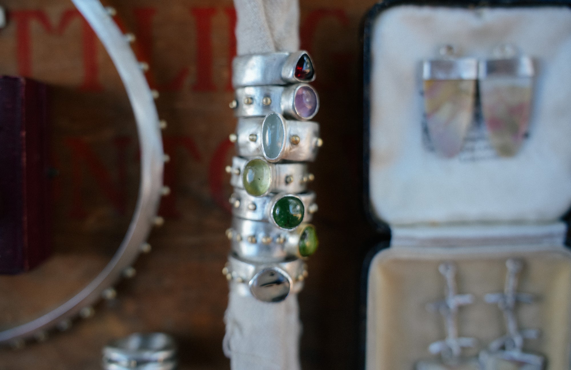 Stack of sterling silver rings with assorted gemstones of different colors on a white surface, with a blurred background