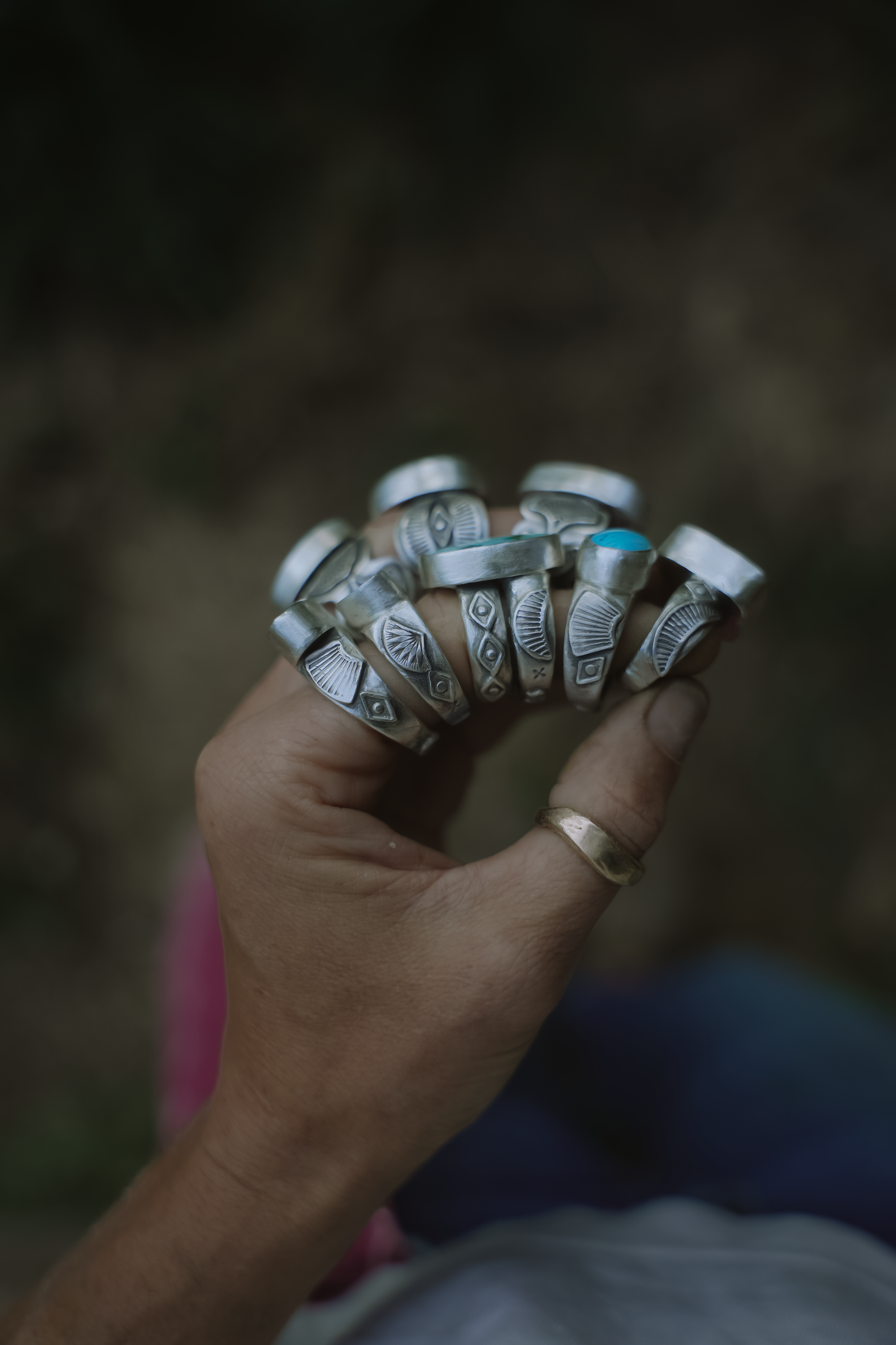A woman's hand wearing multiple silver rings with intricate designs and turquoise stones against a blurred background