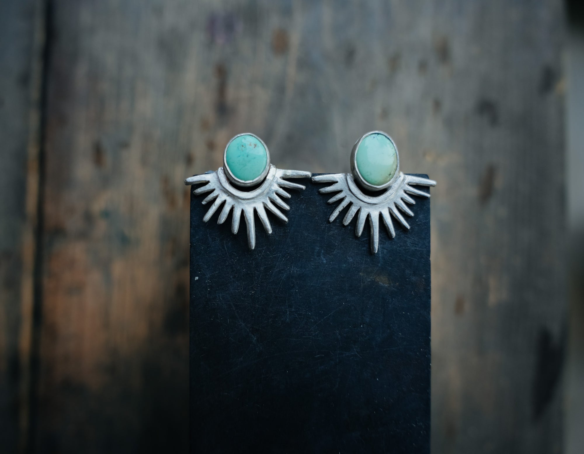 Sterling silver and turquoise post earrings agains a dark background. The silver rays resemble the reflection of the sun’s rays on a lake with the turquoise orbs illustrating the sun.