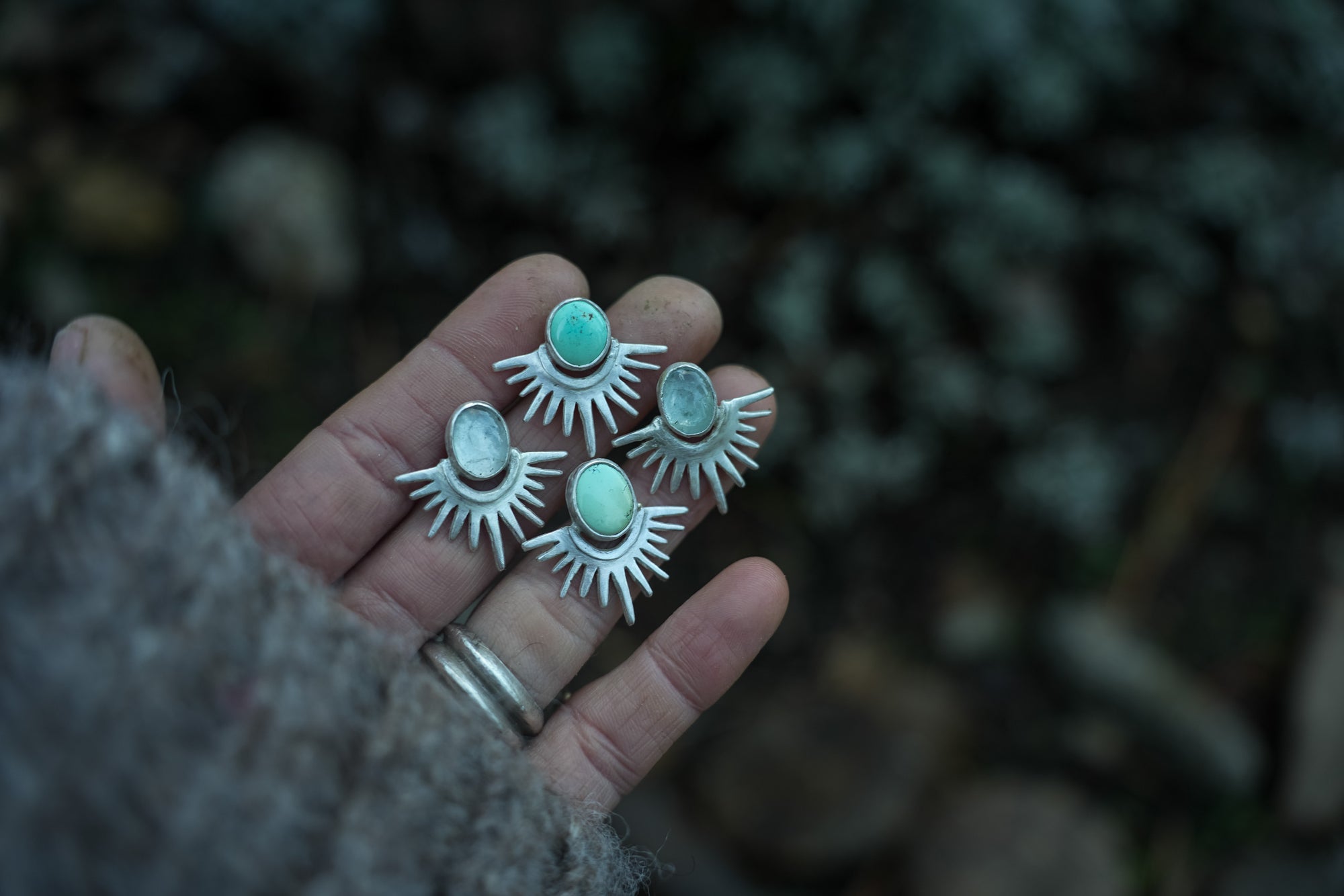 Sterling silver, turquoise, and aquamarine post earrings agains a dark background. The silver rays resemble the reflection of the sun’s rays on a lake with the turquoise orbs illustrating the sun.