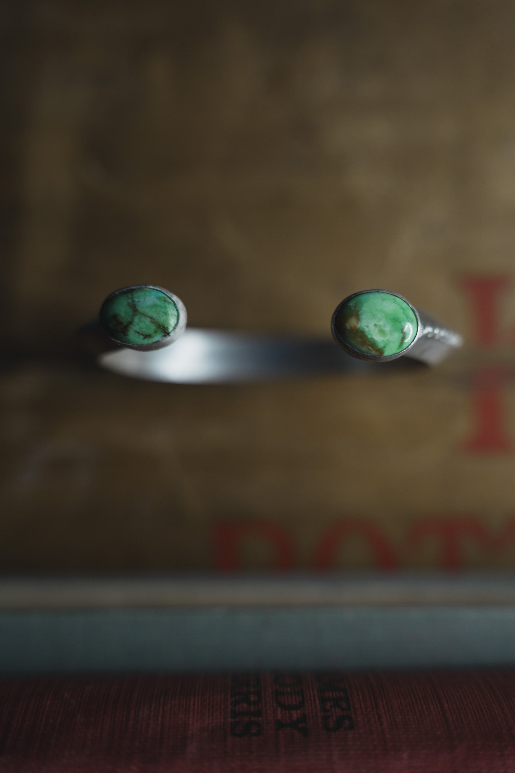 A sterling silver cuff bracelet with oval Sonoran turquoise gemstones at either end balanced on top of a blurred brown background.
