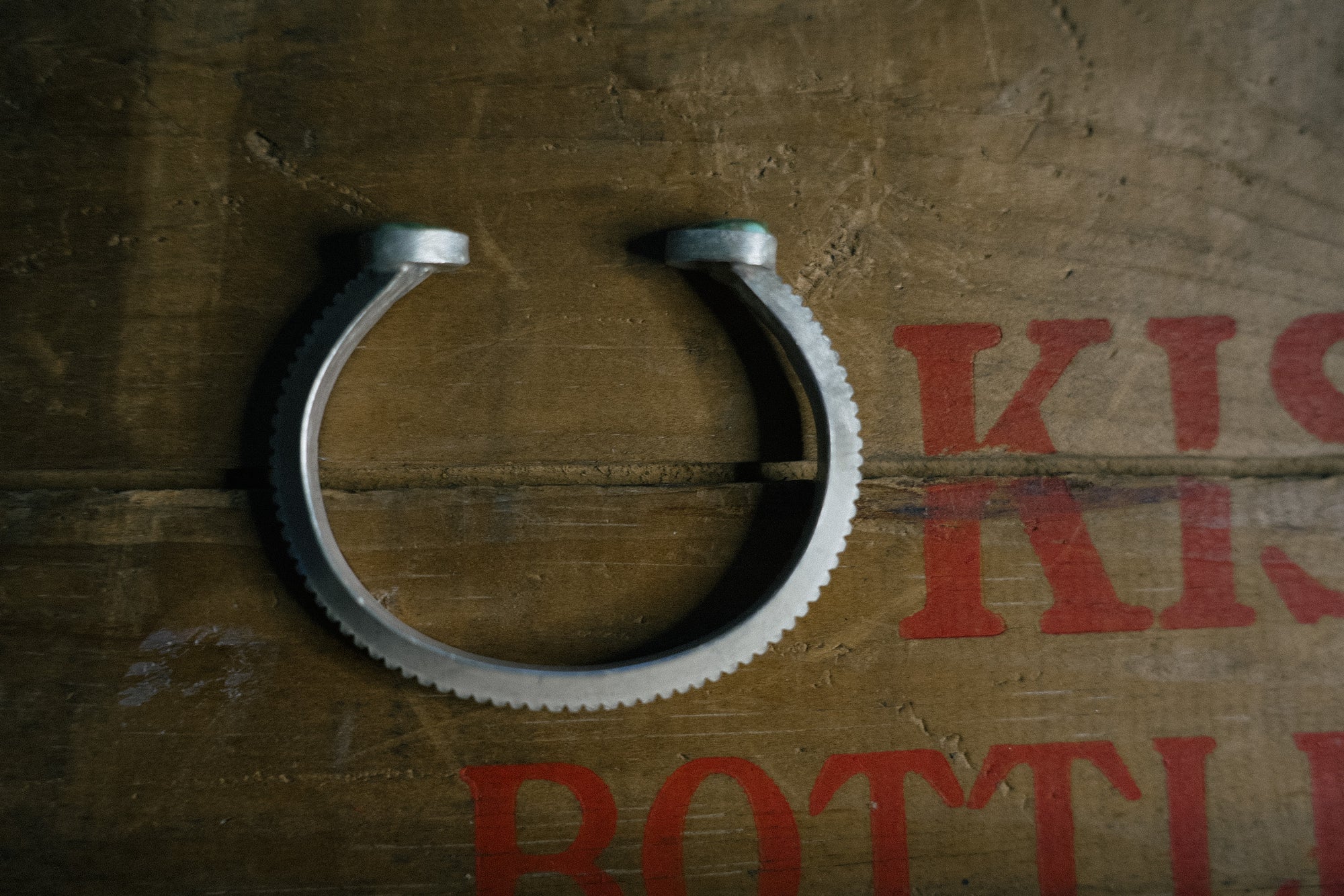 Side view of a thick sterling silver cuff bracelet with green turquoise gemstones at either end. The bracelet edge is serrated.