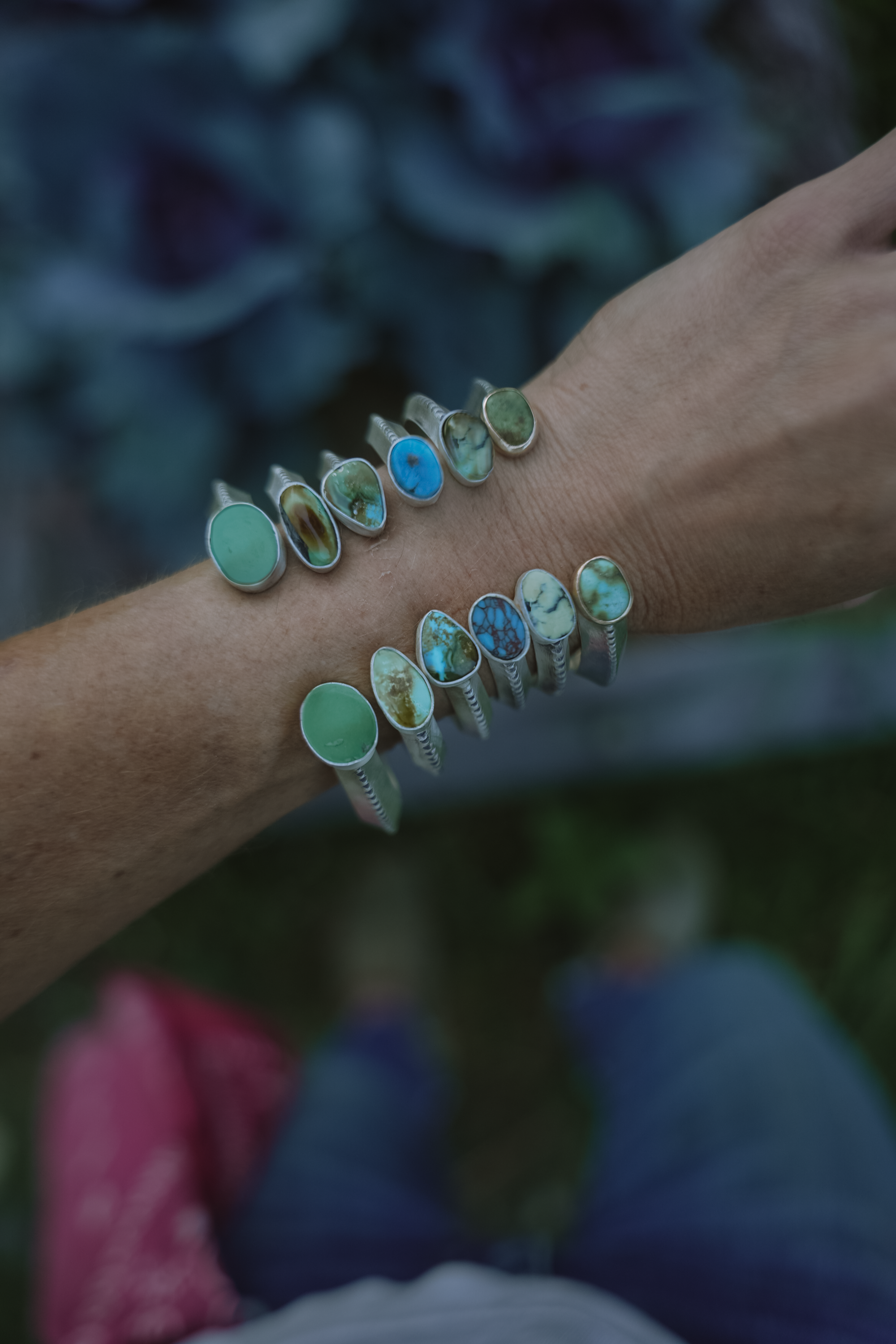 Close-up of a woman's wrist wearing multiple turquoise gemstone and sterling silver bracelets against a blurred background