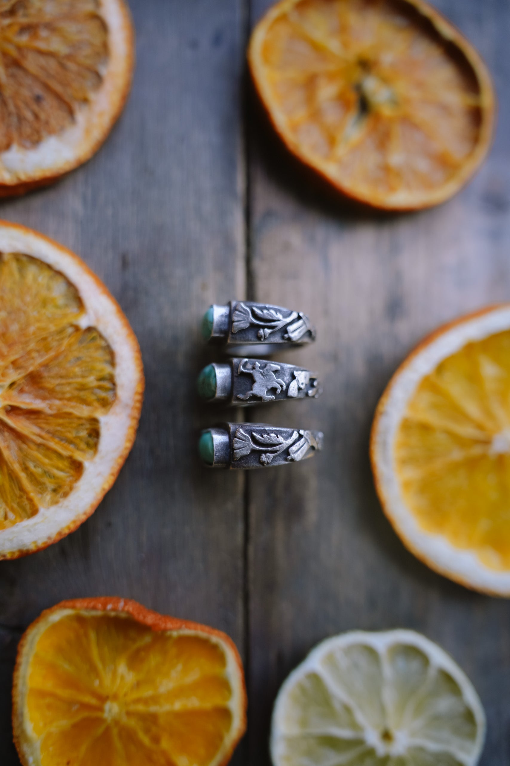 Three sterling silver signet rings with hand-carved Western motifs against a blurred natural background.
