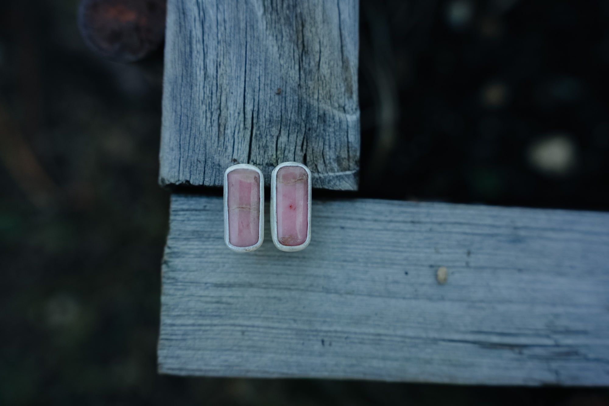 Pair of sterling silver and pink opal bar-shaped earrings on a piece of weathered wood.