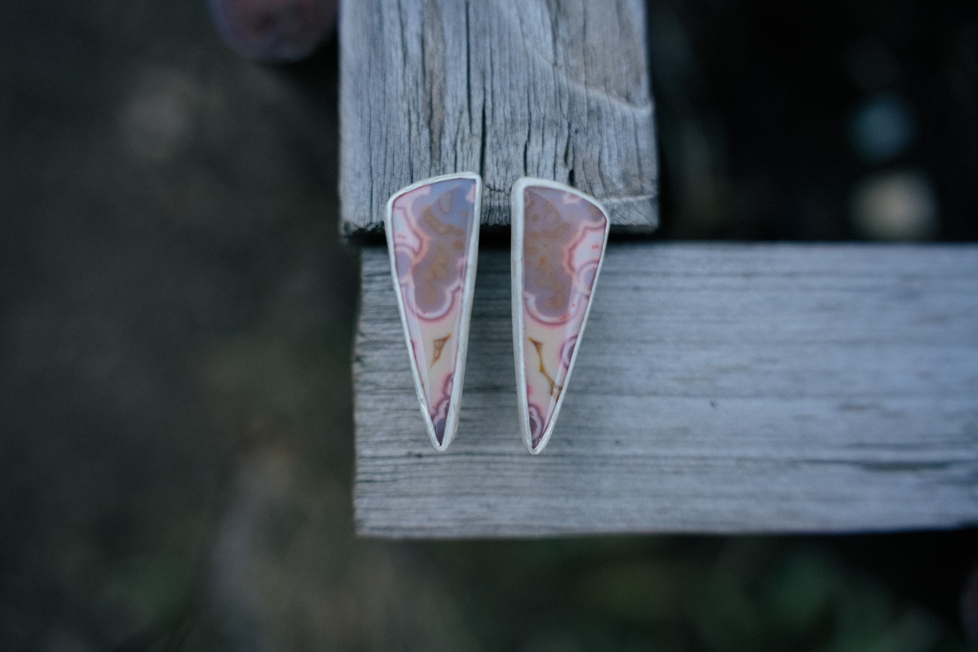 Triangular sterling silver earrings with pink tube agate gemstones set on a wooden surface