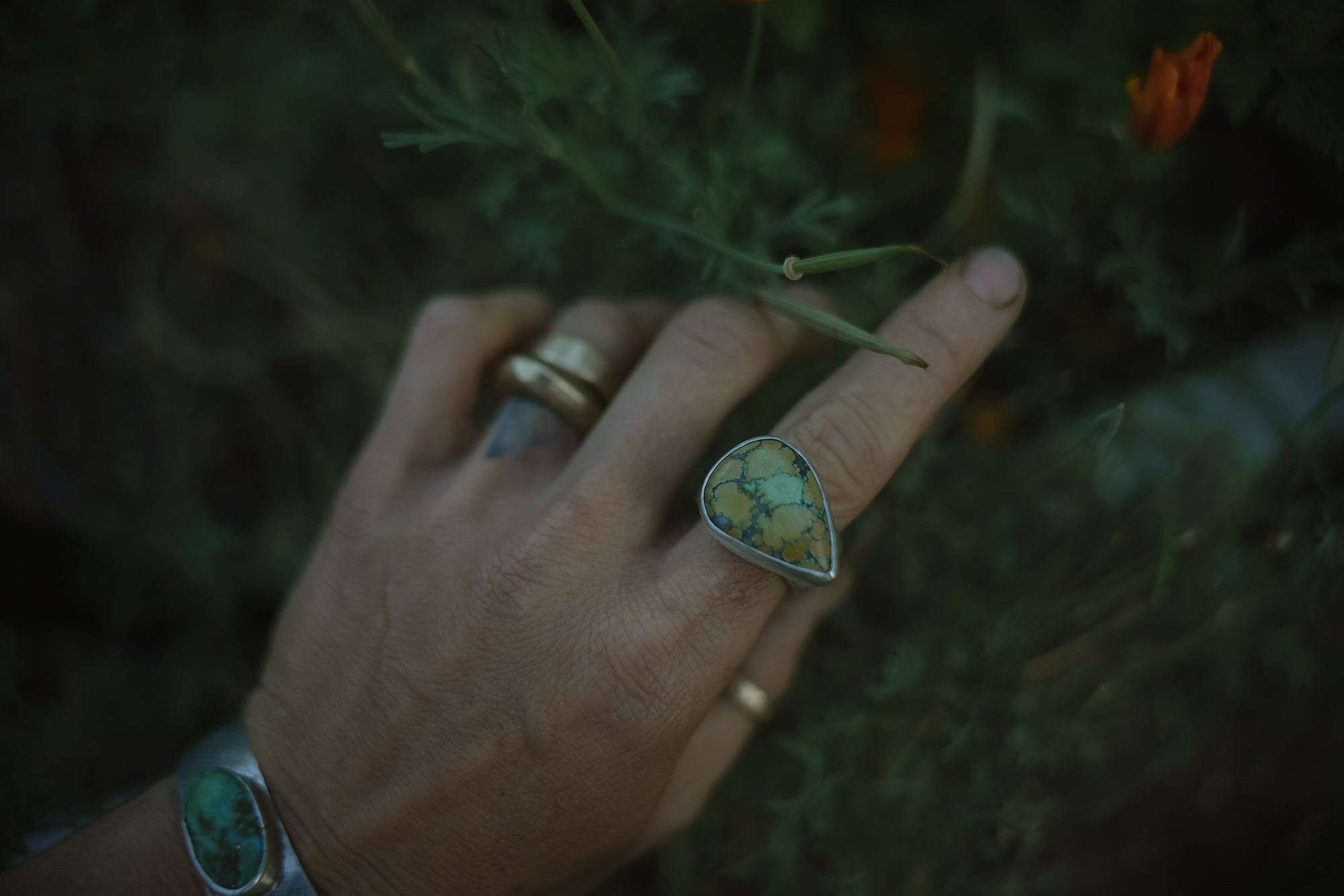 A woman's hand wearing a sterling silver ring with a turquoise stone against a natural background