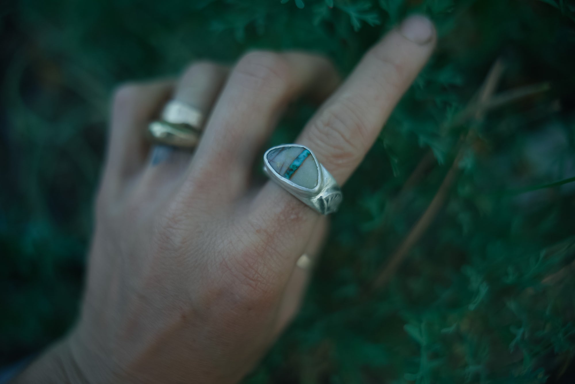 Hand wearing a silver ring with a blue stone against a blurred green background