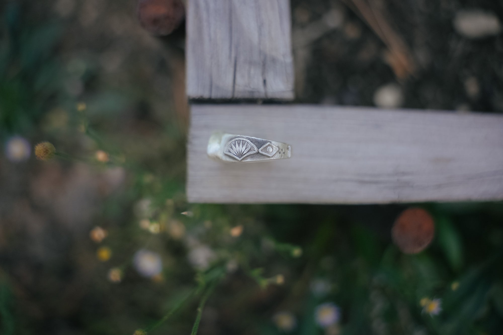 Silver ring with a unique hand-stamped design on a wooden surface with a blurred natural background