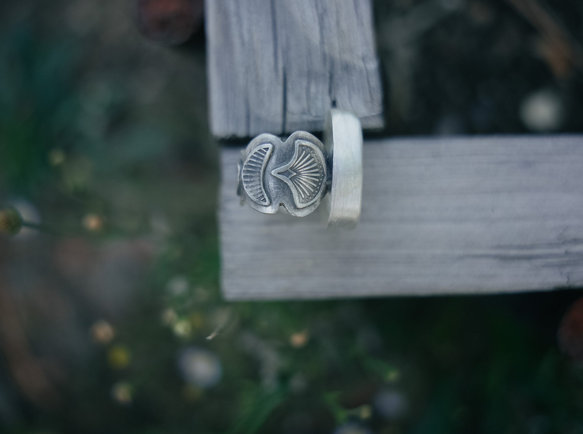 Sterling silver ring with a wide hand-stamped band against a wooden block against a blurred natural background