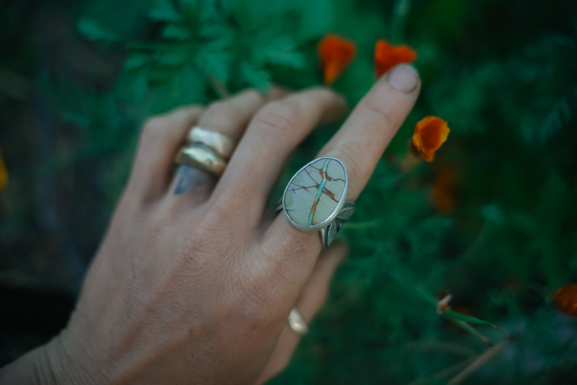 A woman's hand wearing a sterling silver and Royston Ribbon turquoise ring against a blurred natural background