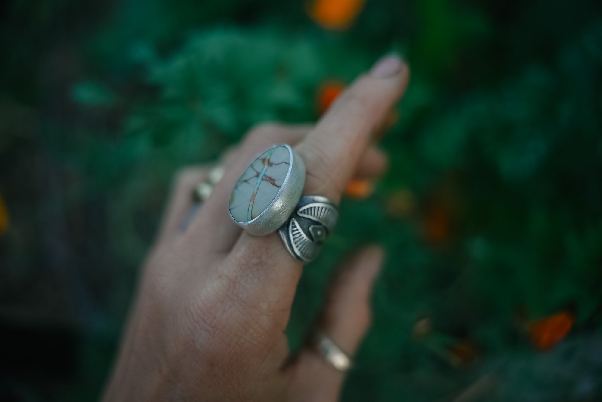 A woman's hand wearing a sterling silver ring with a Royston Ribbon turquoise stone against a blurred green background