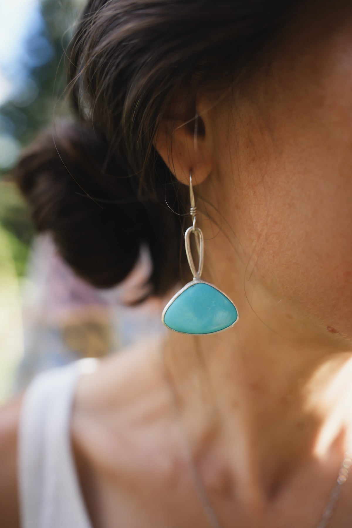 A close-up lifestyle shot of a woman wearing a silver dangle earring with a smooth, organic-shaped light blue turquoise gemstone.