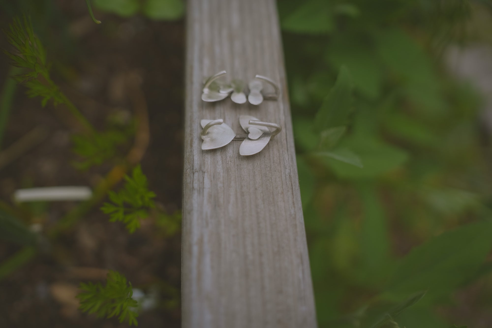 A pair of floral sterling silver Birkenstock shoe clips on a wooden board, against a blurred green background. The flower style is folk art. The shoe clips are positioned to show the backside.