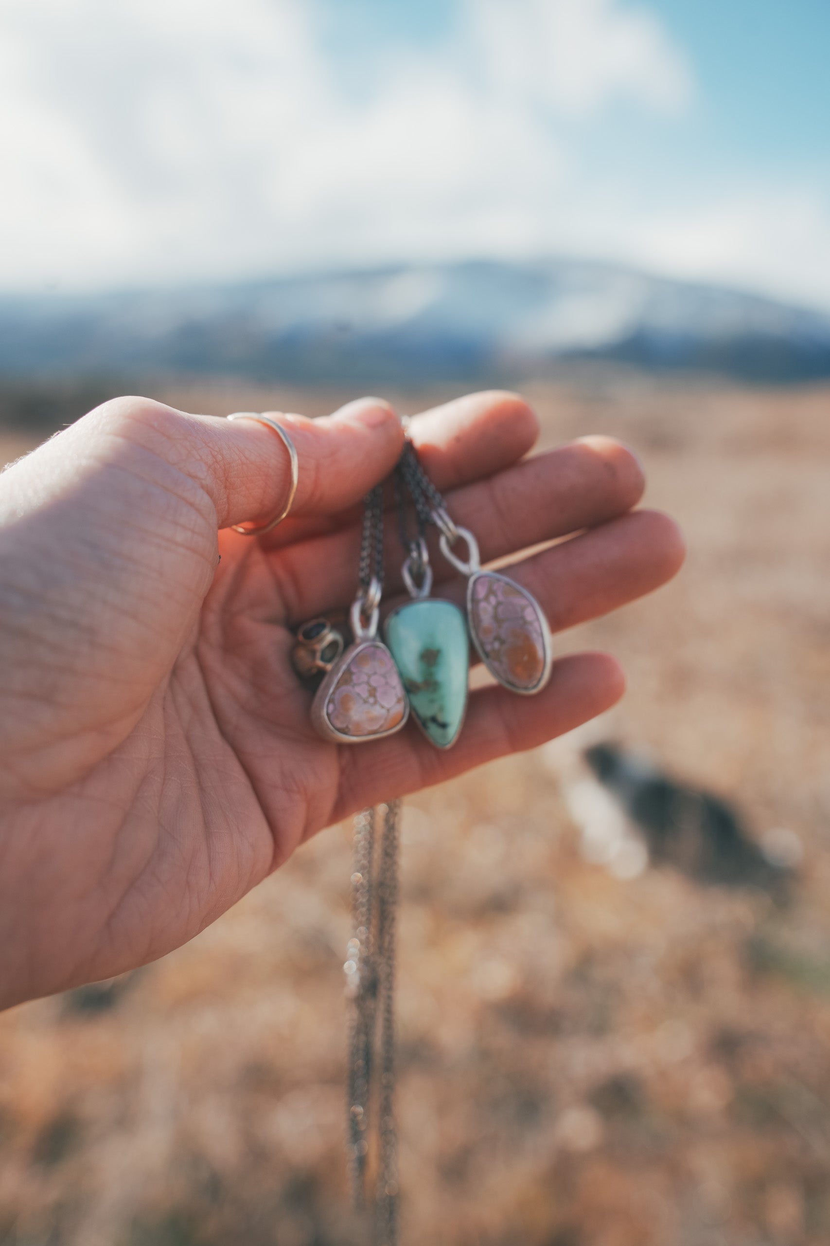A woman's hand holding three sterling silver necklaces with gemstone pendants against a blurred natural background