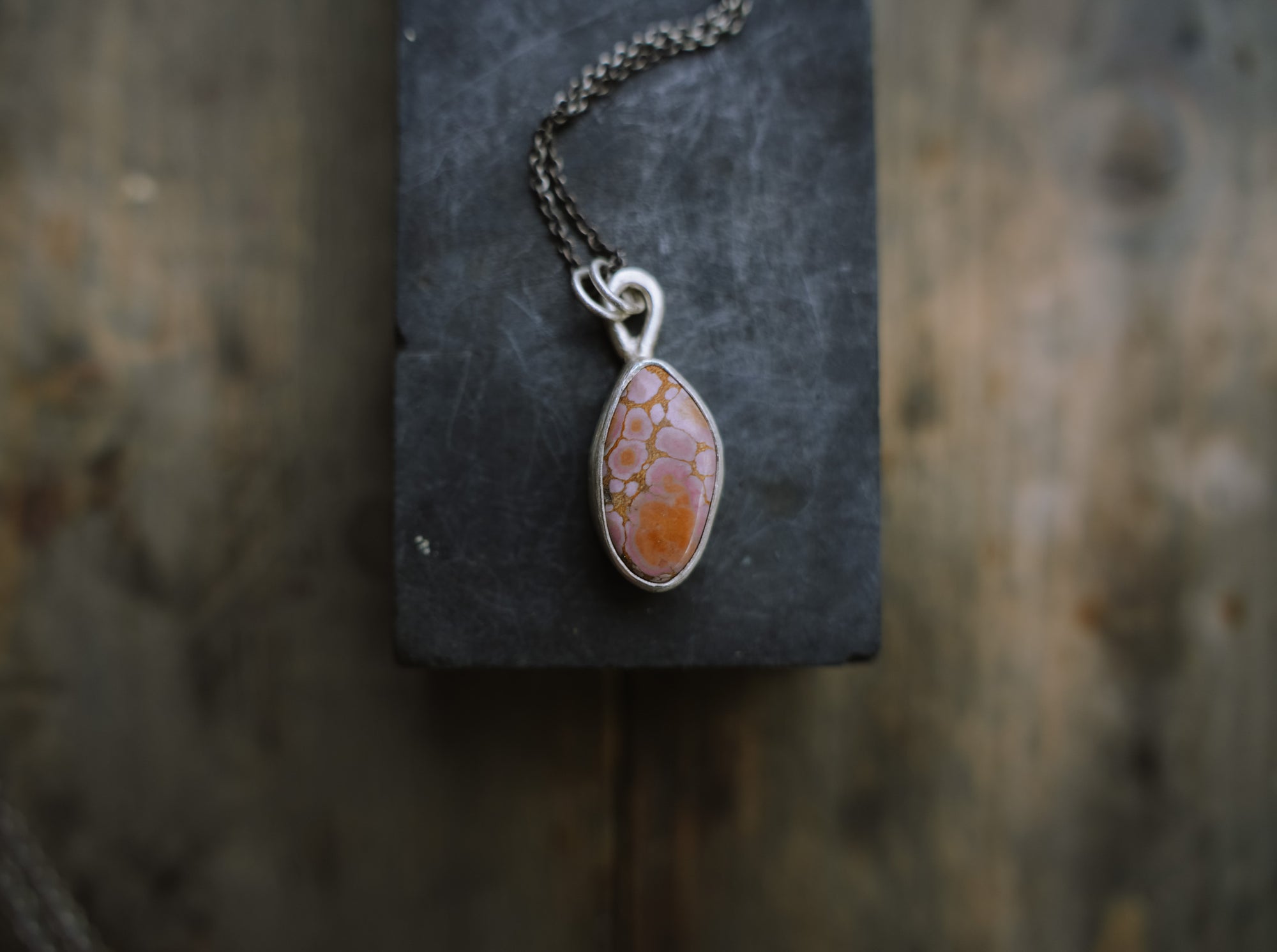 Sterling silver necklace with a triangular pink and orange gemstone pendant against a dark textured surface.