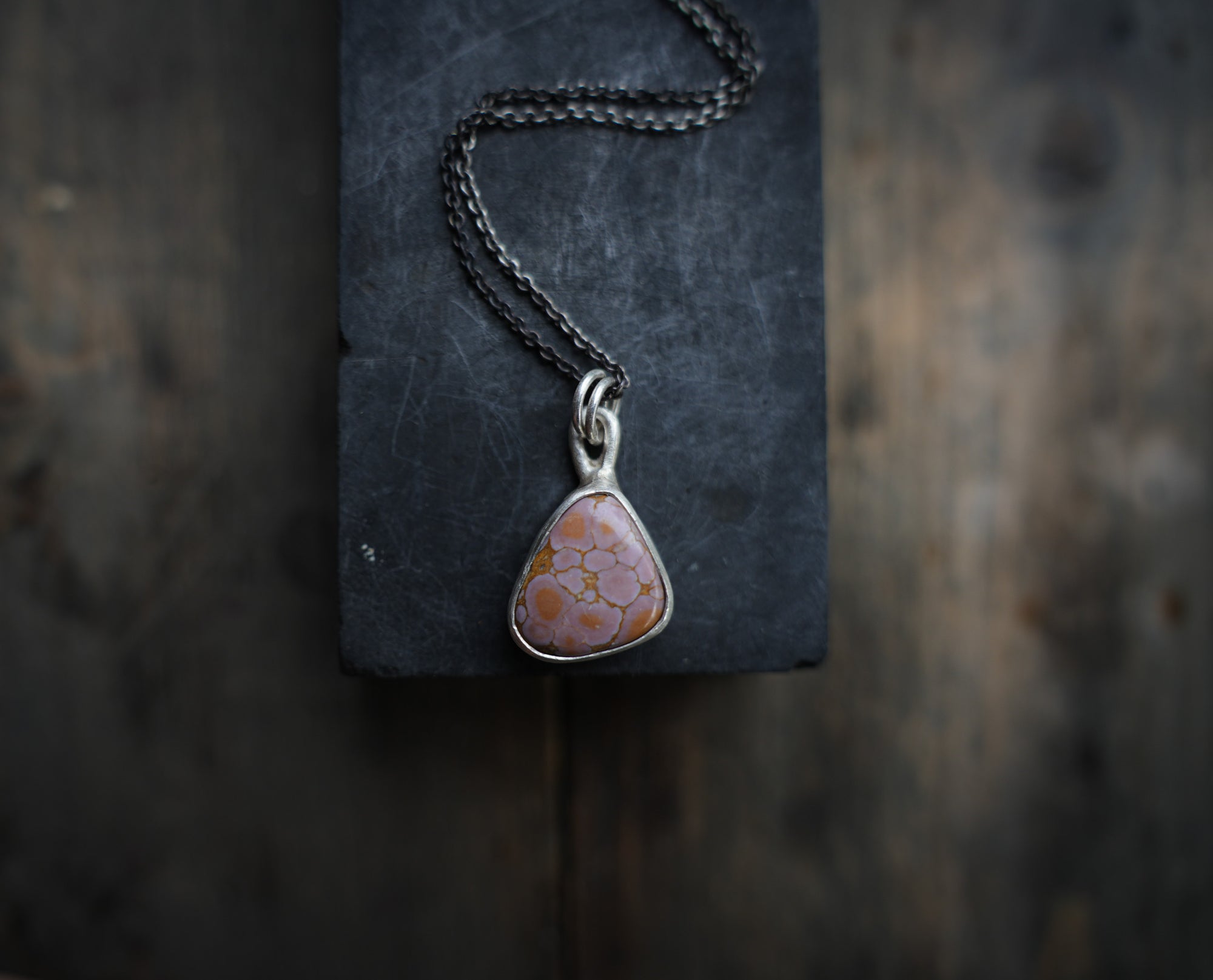 Sterling silver necklace with a triangular pink opal gemstone pendant on a dark textured surface.