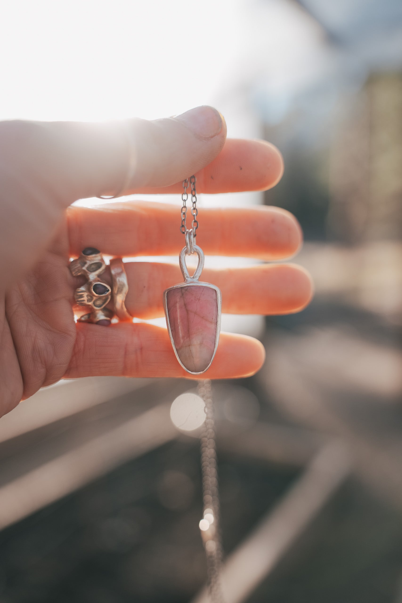 A woman's hand holding a sterling silver and pink opal shield-shaped pendant on a sterling silver chain.