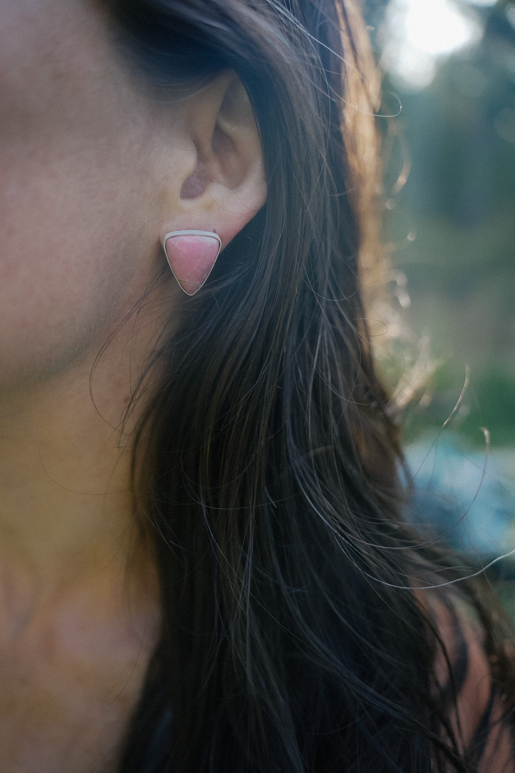 Close-up of a woman wearing a pair of sterling silver and pink opal triangular-shaped earrings against a blurred background