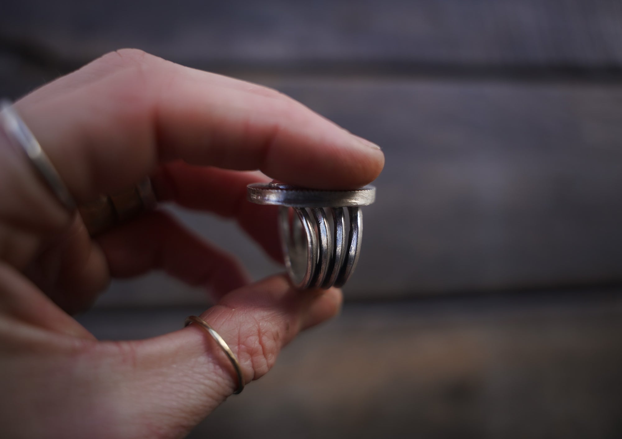 A woman's hand holding a sterling silver ring with a pink opal against a blurred natural background. This is a side-view to show the wide band which is comprised of four narrow bands.