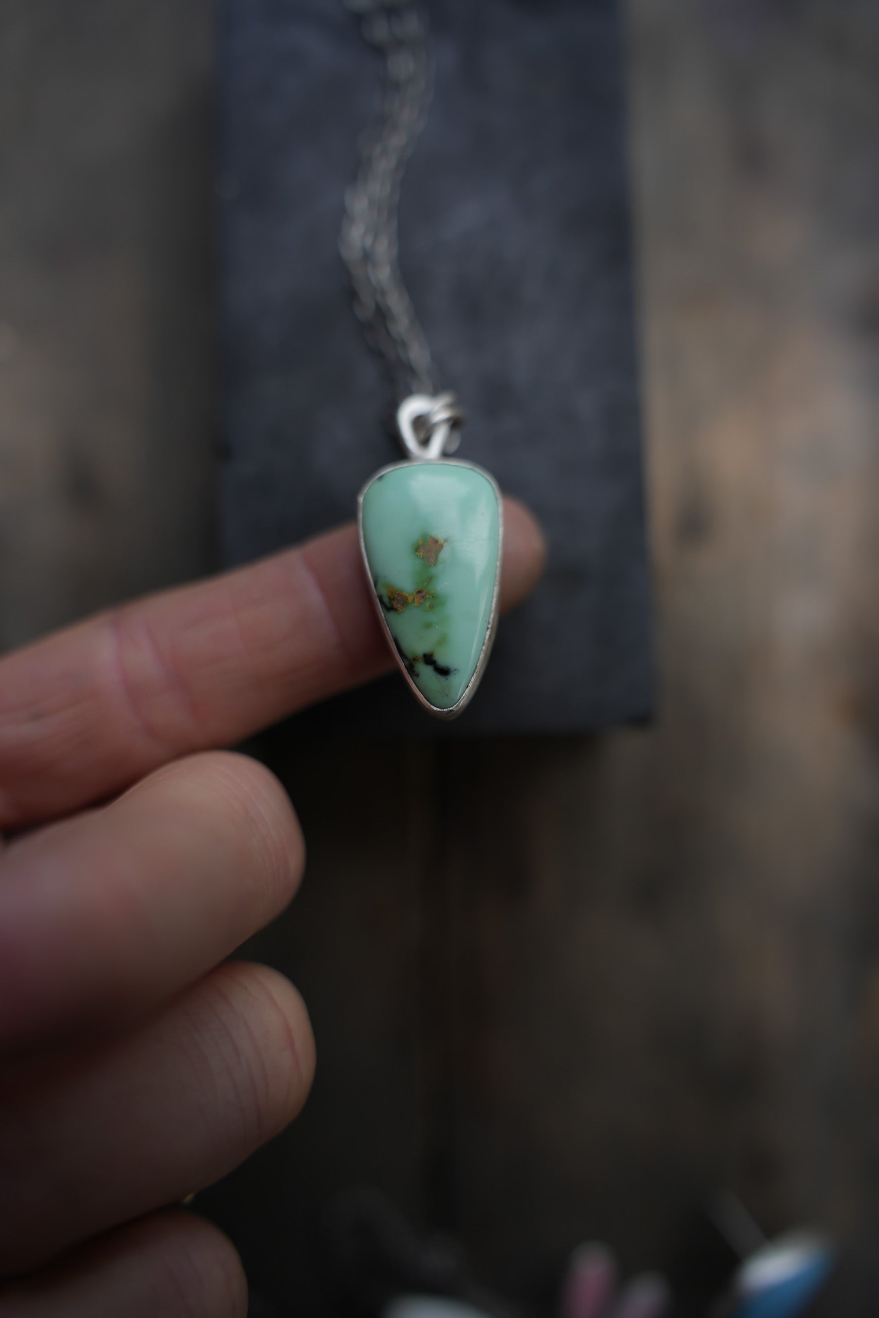 Sterling silver and blue-green turquoise pendant necklace set on a woman's forefinger against a dark background. The pendant is shaped like a rounded inverted triangle.