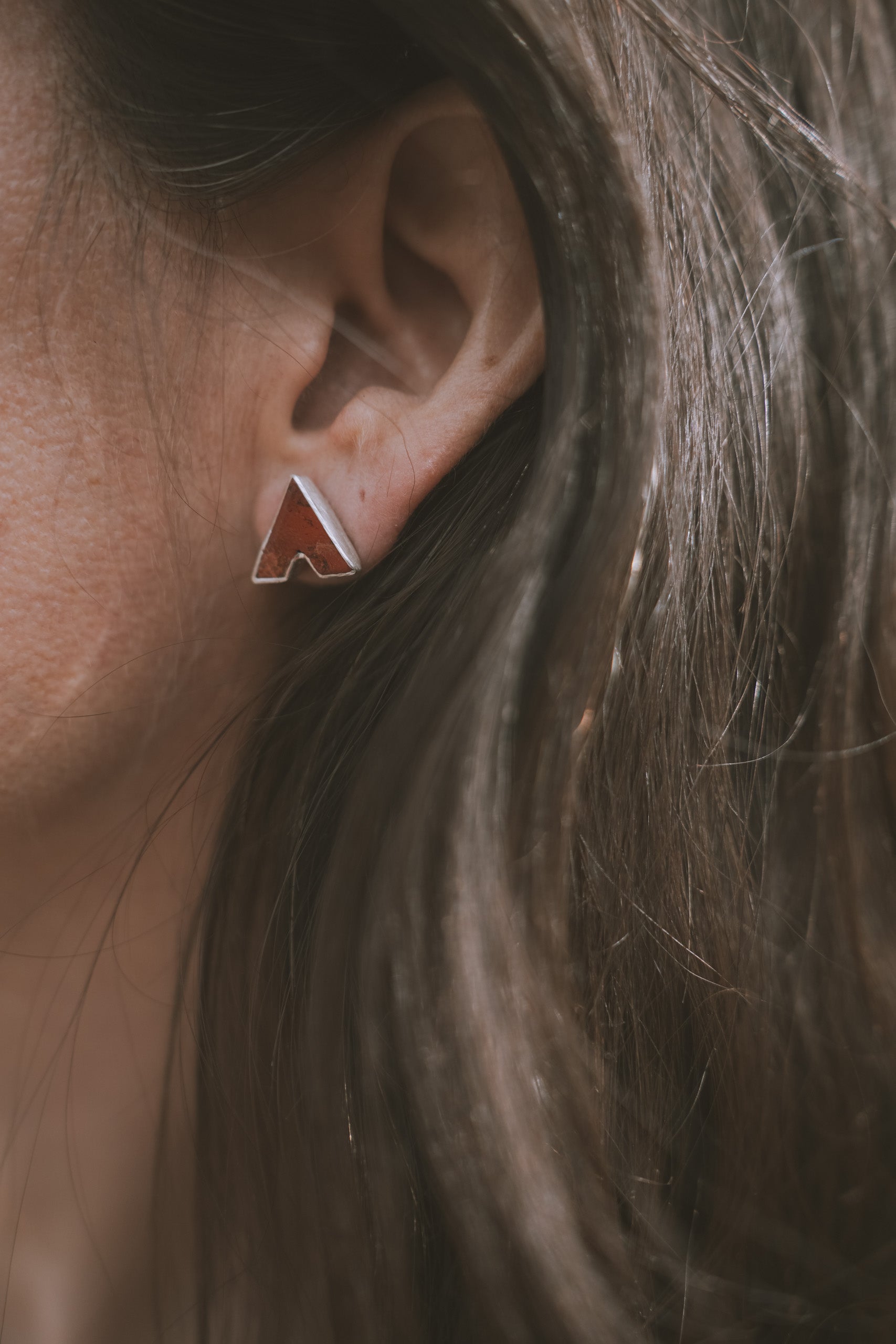 Close-up of a woman wearing a sterling silver and red poppy jasper V-shaped post earring. 
