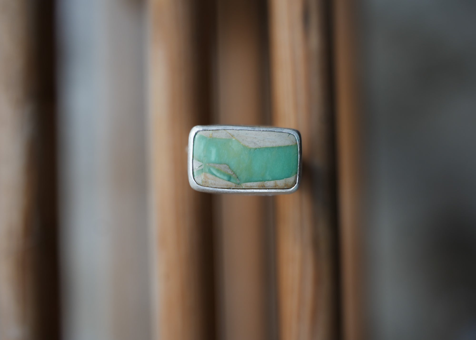 A sterling silver ring with a rectangular aqua and cream varoscite gemstone on a blurred background gemstone against a blurred background.