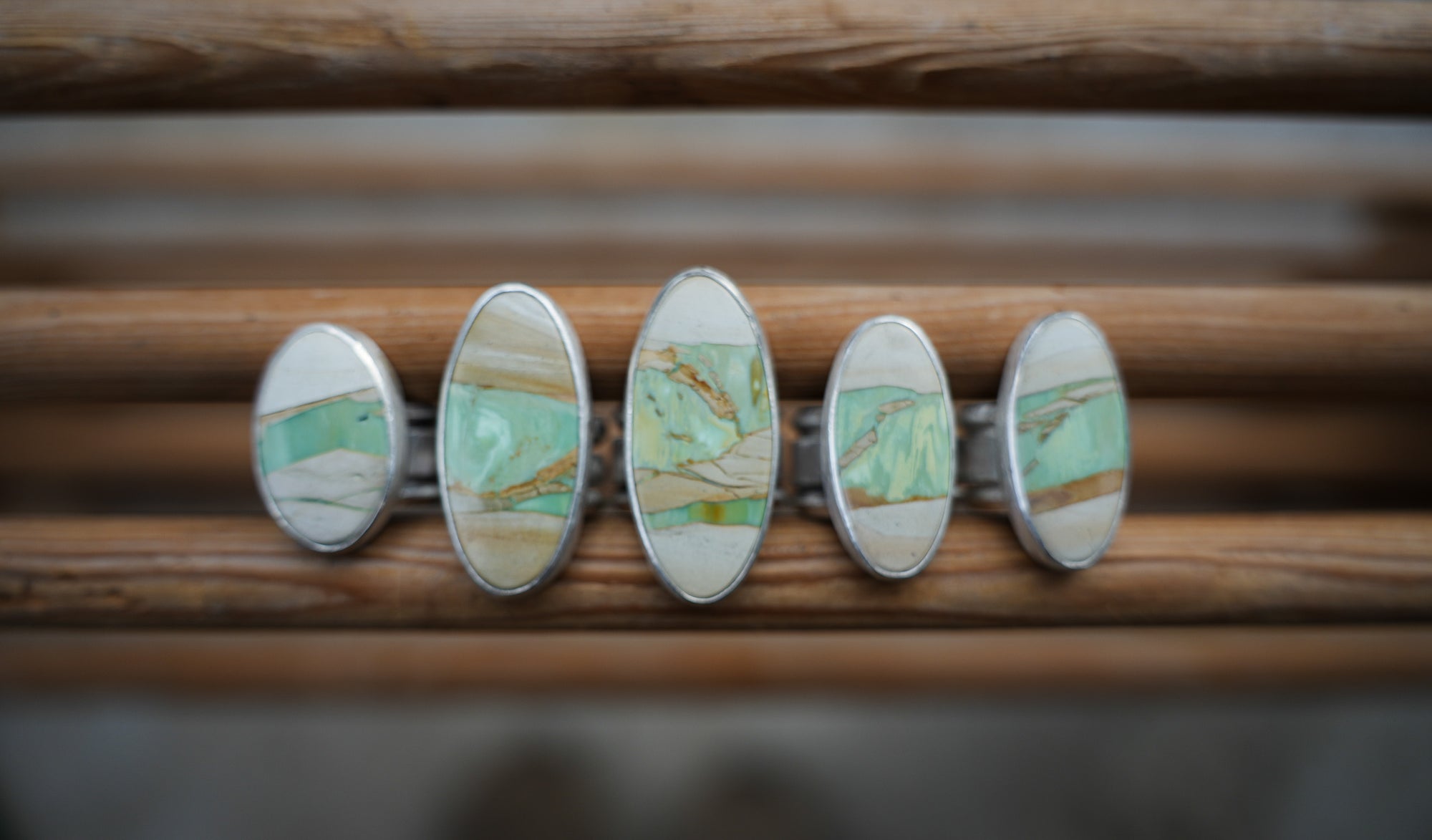 Five oval-shaped sterling silver rings with aqua, cream, and brown variscite gemstones against a wooden surface.
