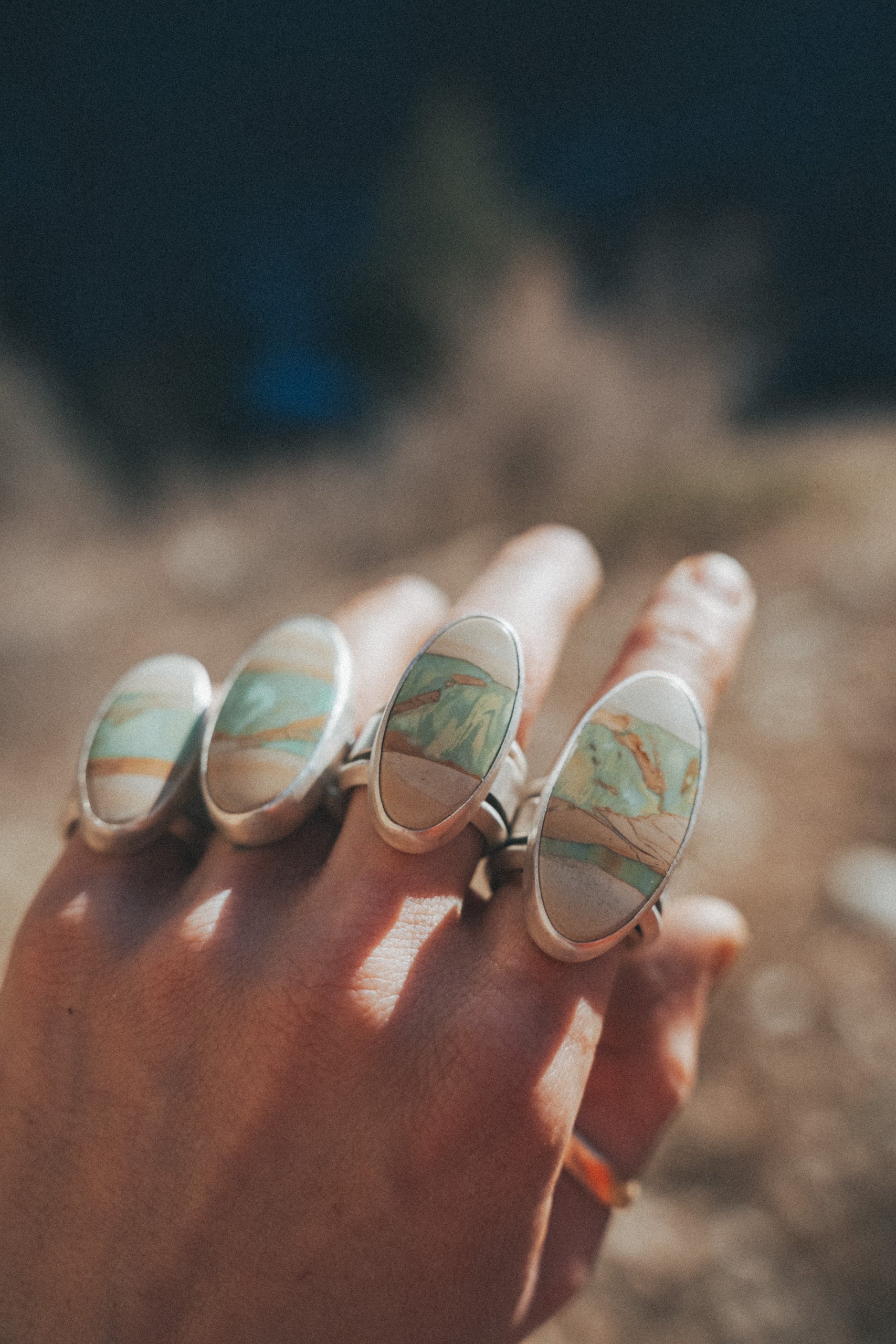 A woman's hand has four sterling silver rings, one on each finger. Each ring has an oval green and cream. and light brown variscite gemstone. The sterling silver bands are wide.