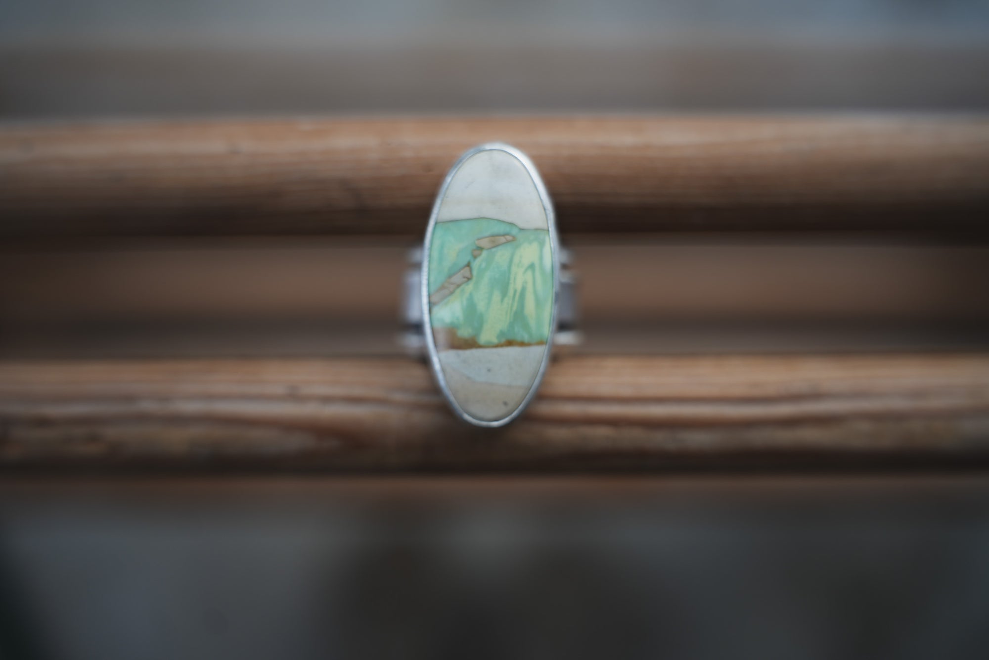 A sterling silver wide-band ring with an oval variscite gemstone, set on a wooden surface.