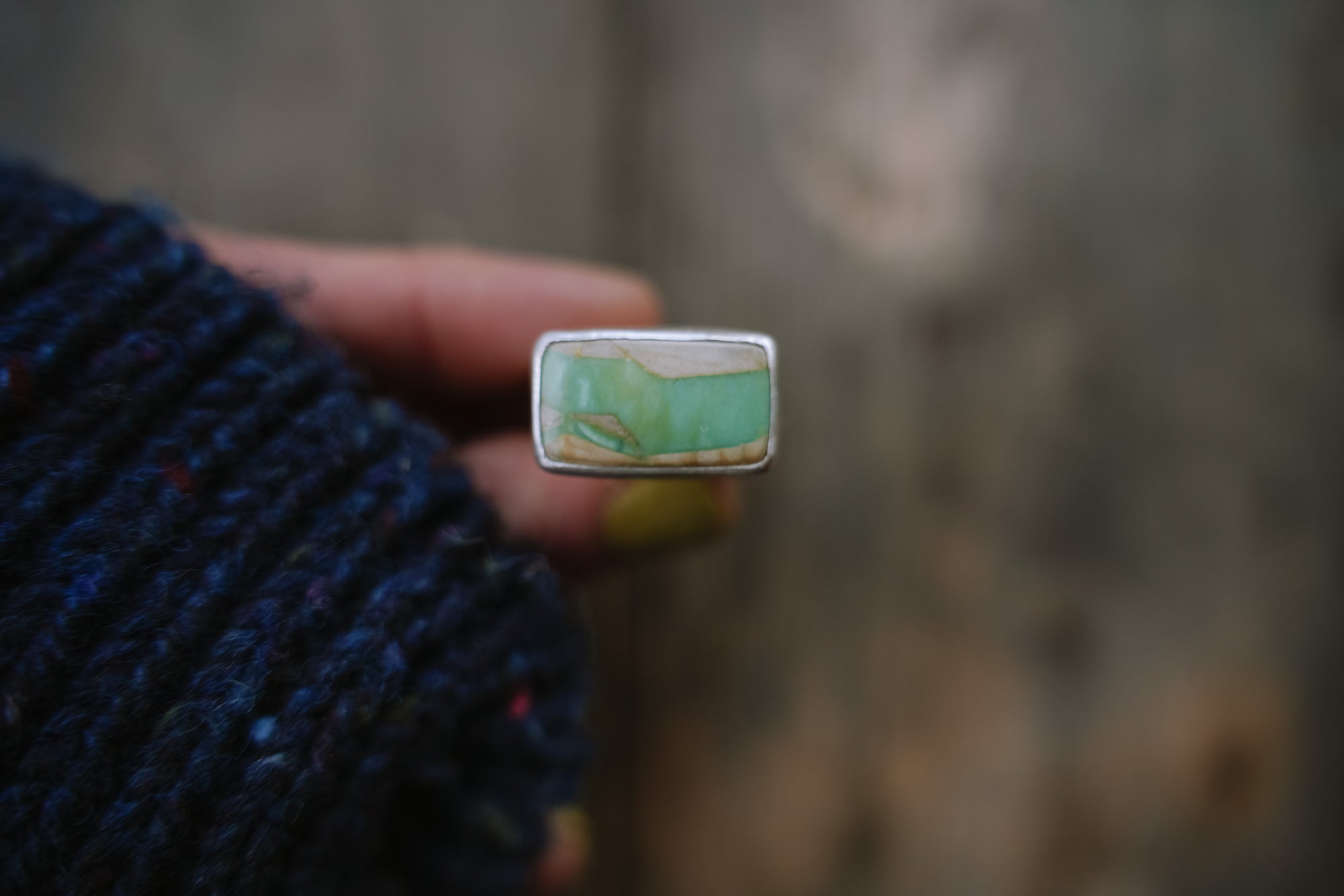 A woman's hand holding a sterling silver ring with a rectangular green-and-cream gemstone.