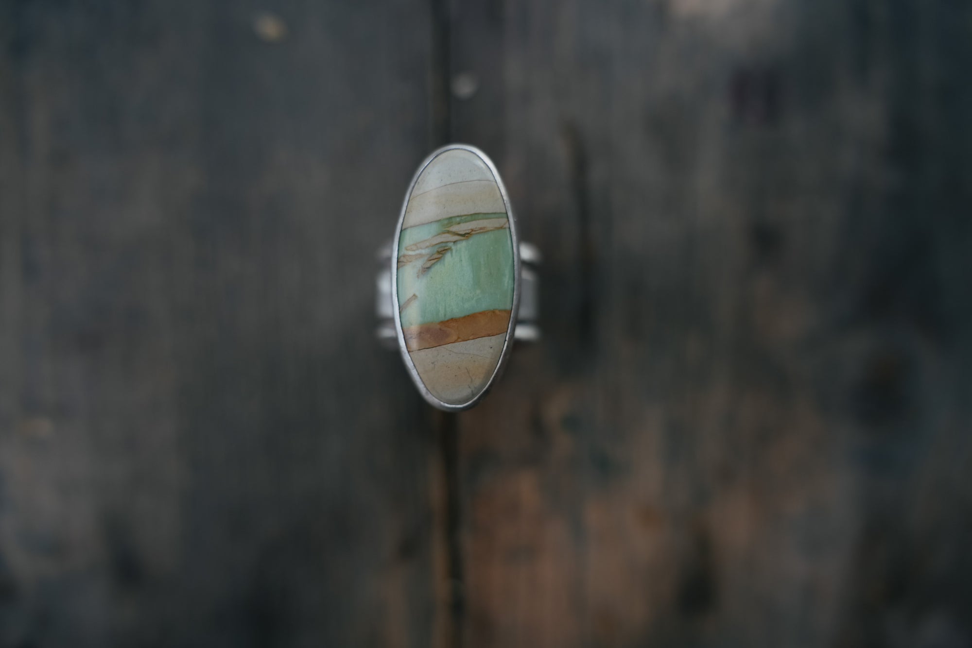A sterling silver ring with an oval pale green, cream, and warm brown gemstone on a dark wooden surface.
