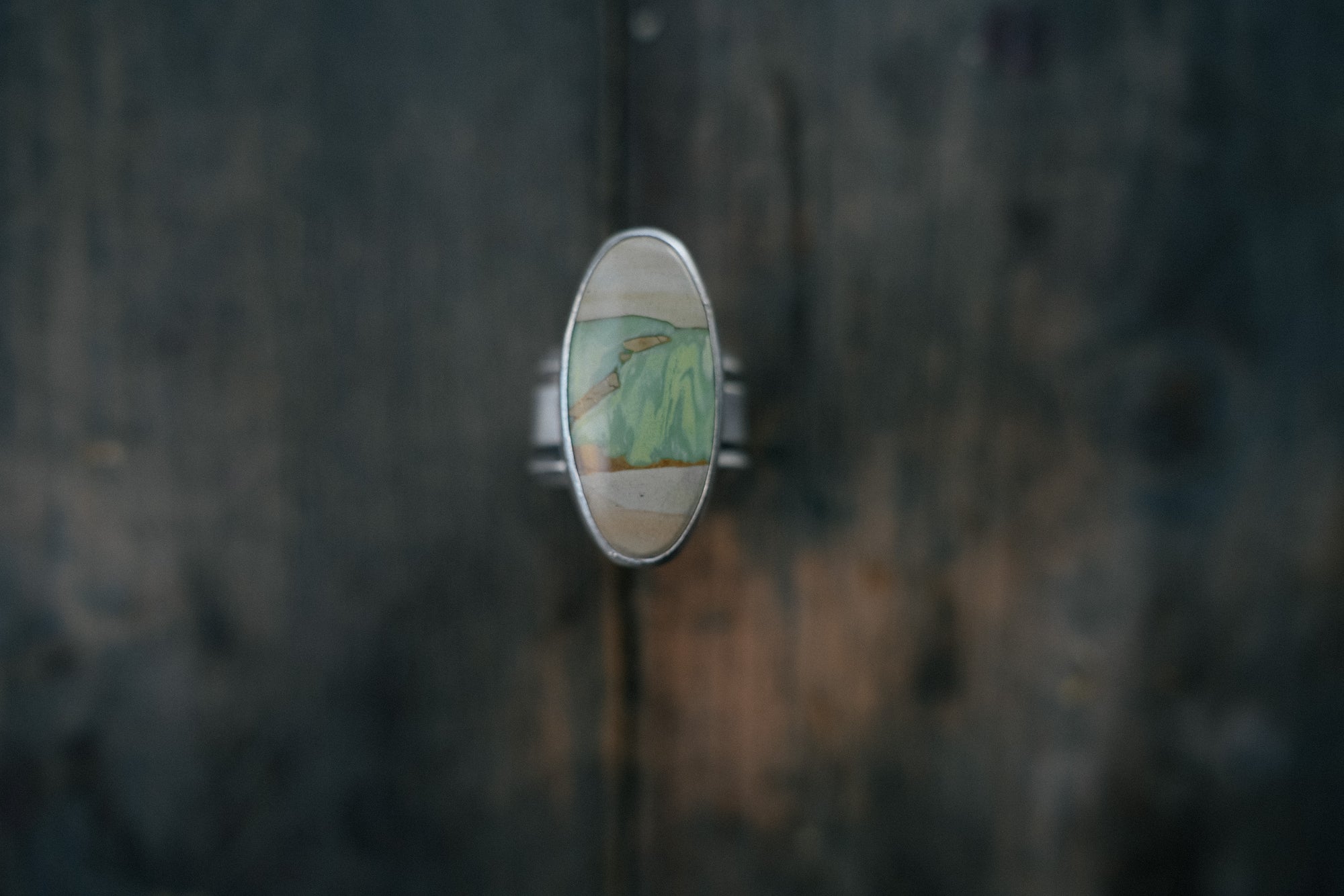 A sterling silver ring with an oval pale green, cream, and warm brown gemstone on a dark wooden surface.