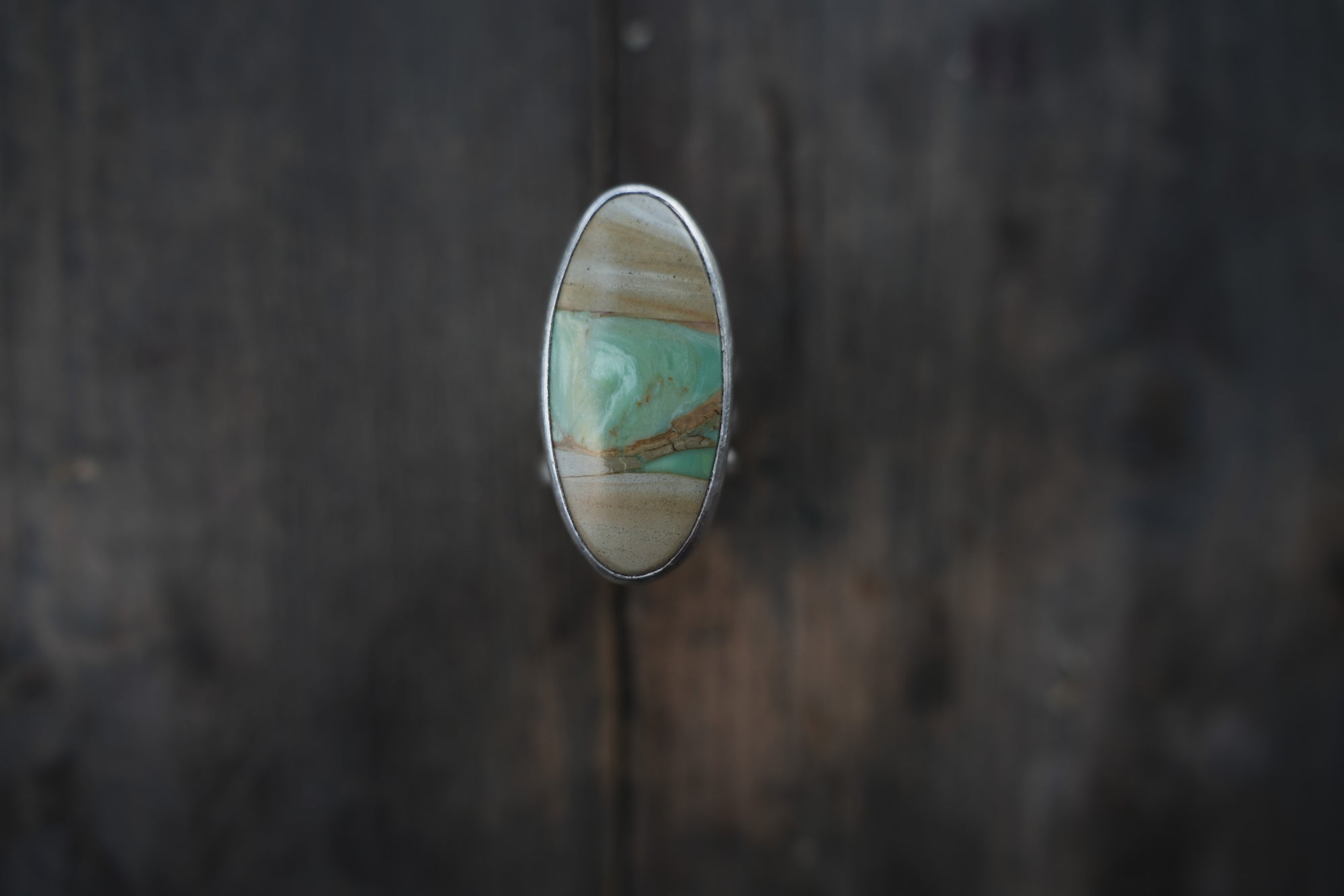 A sterling silver ring with an oval pale green, cream, and warm brown gemstone on a dark wooden surface