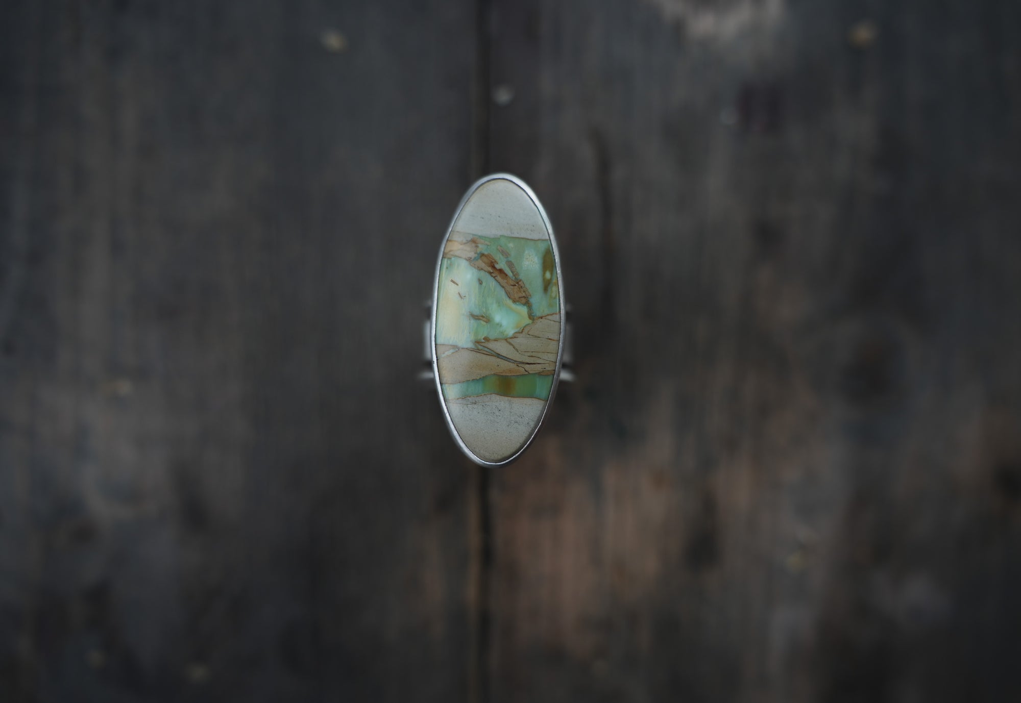 A sterling silver ring with an oval pale green, cream, and warm brown gemstone on a dark wooden surface