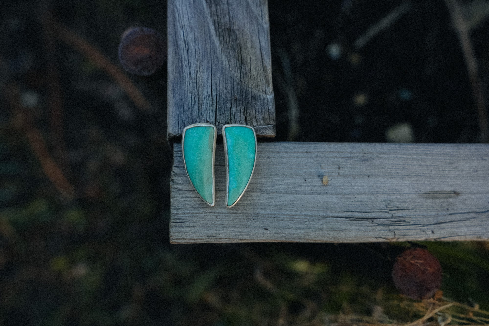 Turquoise and solver talon-shaped earrings on a wooden surface with a blurred natural background