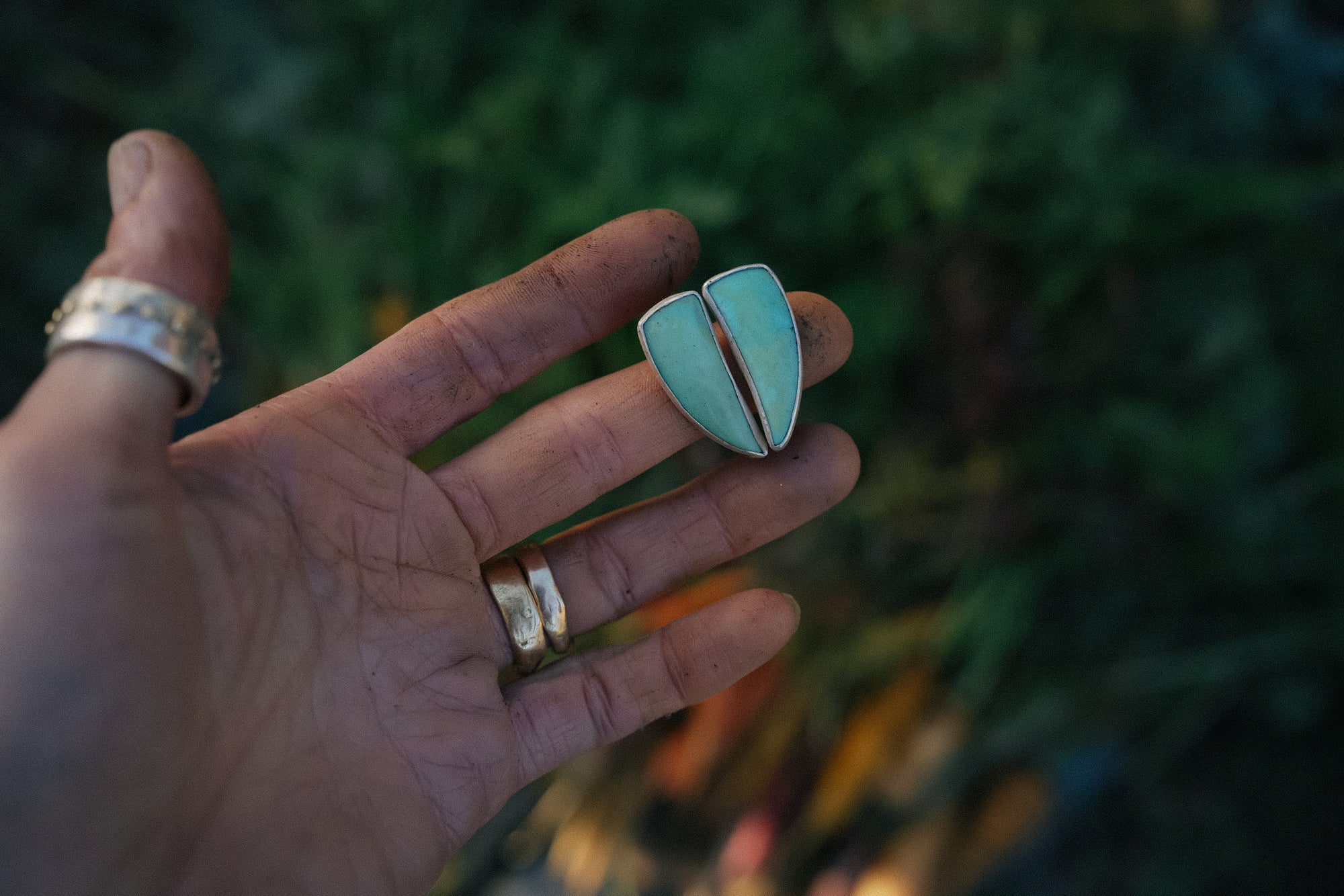 Hand holding a pair of turquoise and silver talon-shaped earrings against a blurred background.