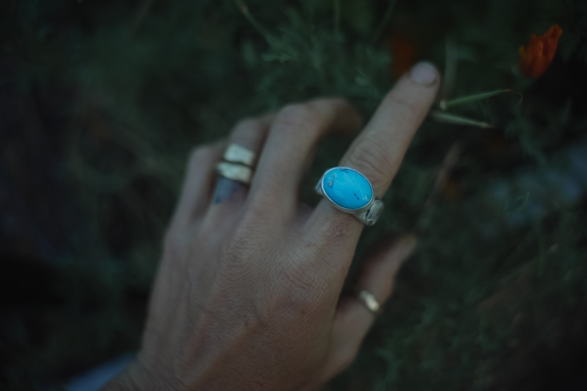 A woman's hand wearing a sterling silver and turquoise ring against a blurred natural background