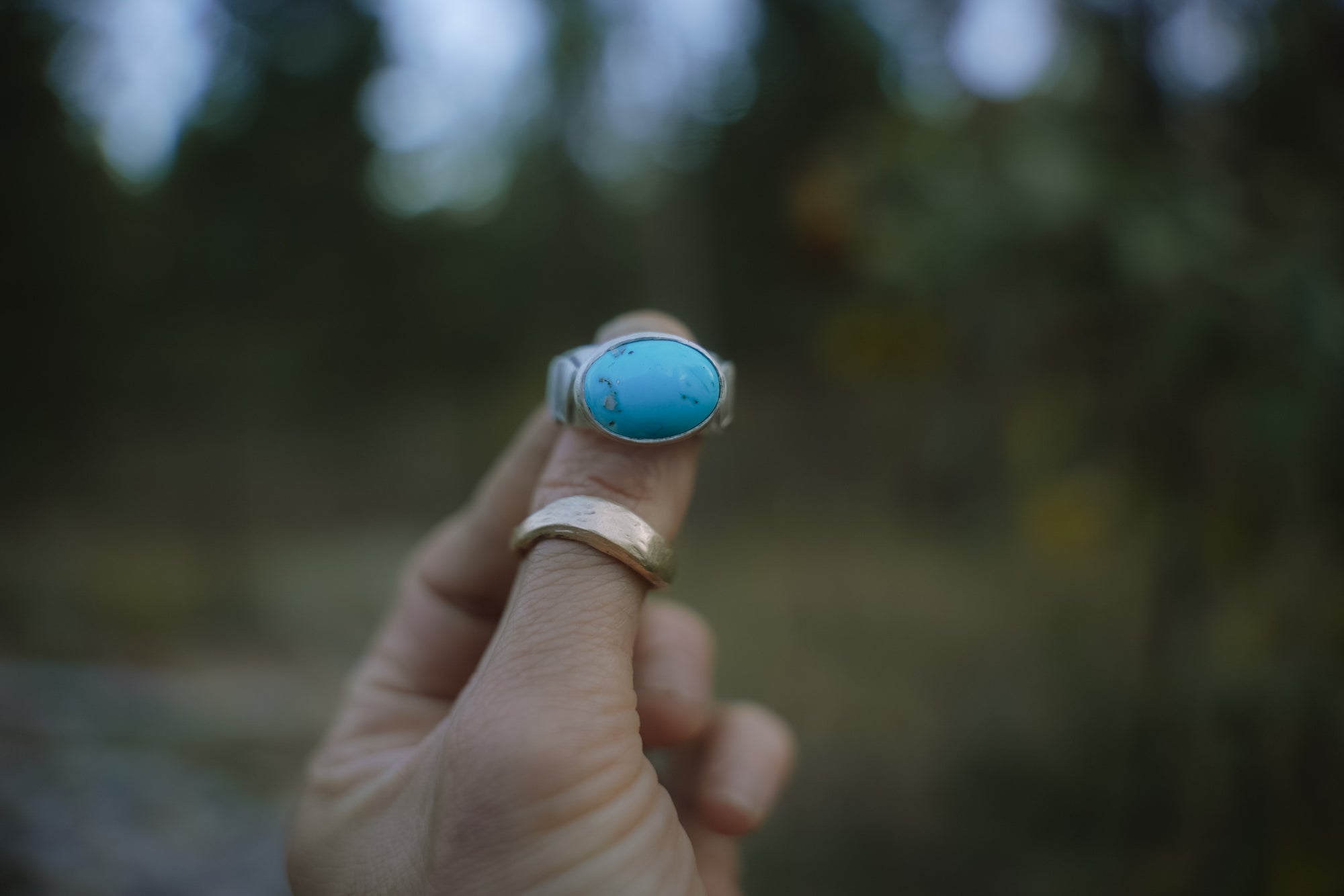 Hand holding a turquoise and sterling silver ring with a blurred natural background