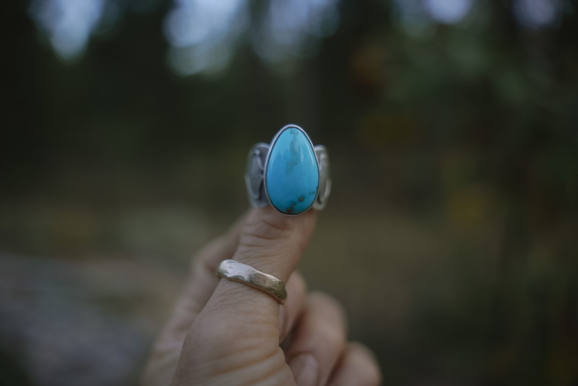 Sterlign silver and turquoise ring held by a hand with a blurred natural background